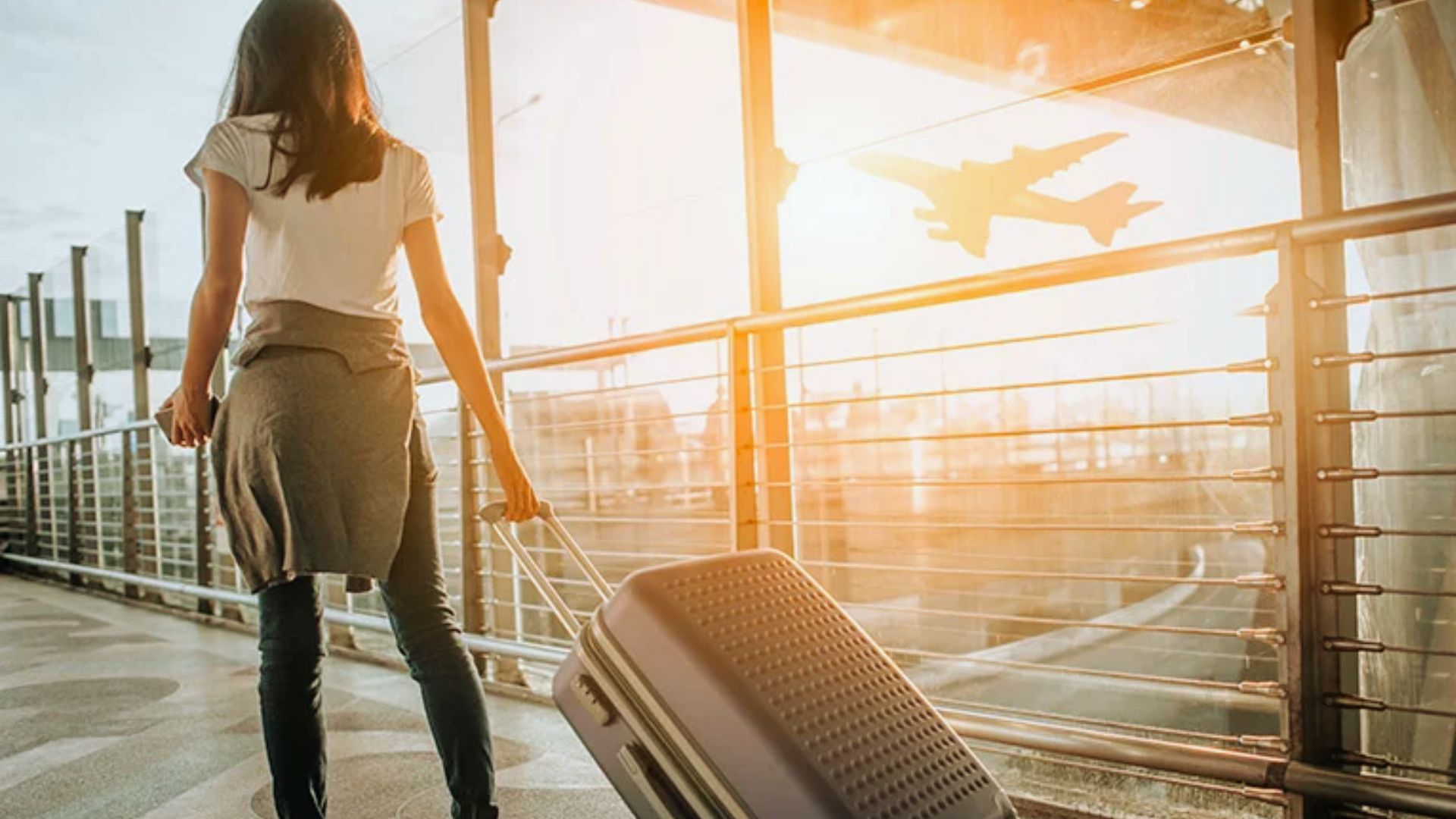 A woman with a suitcase waits at the airport, looking towards her departure gate.