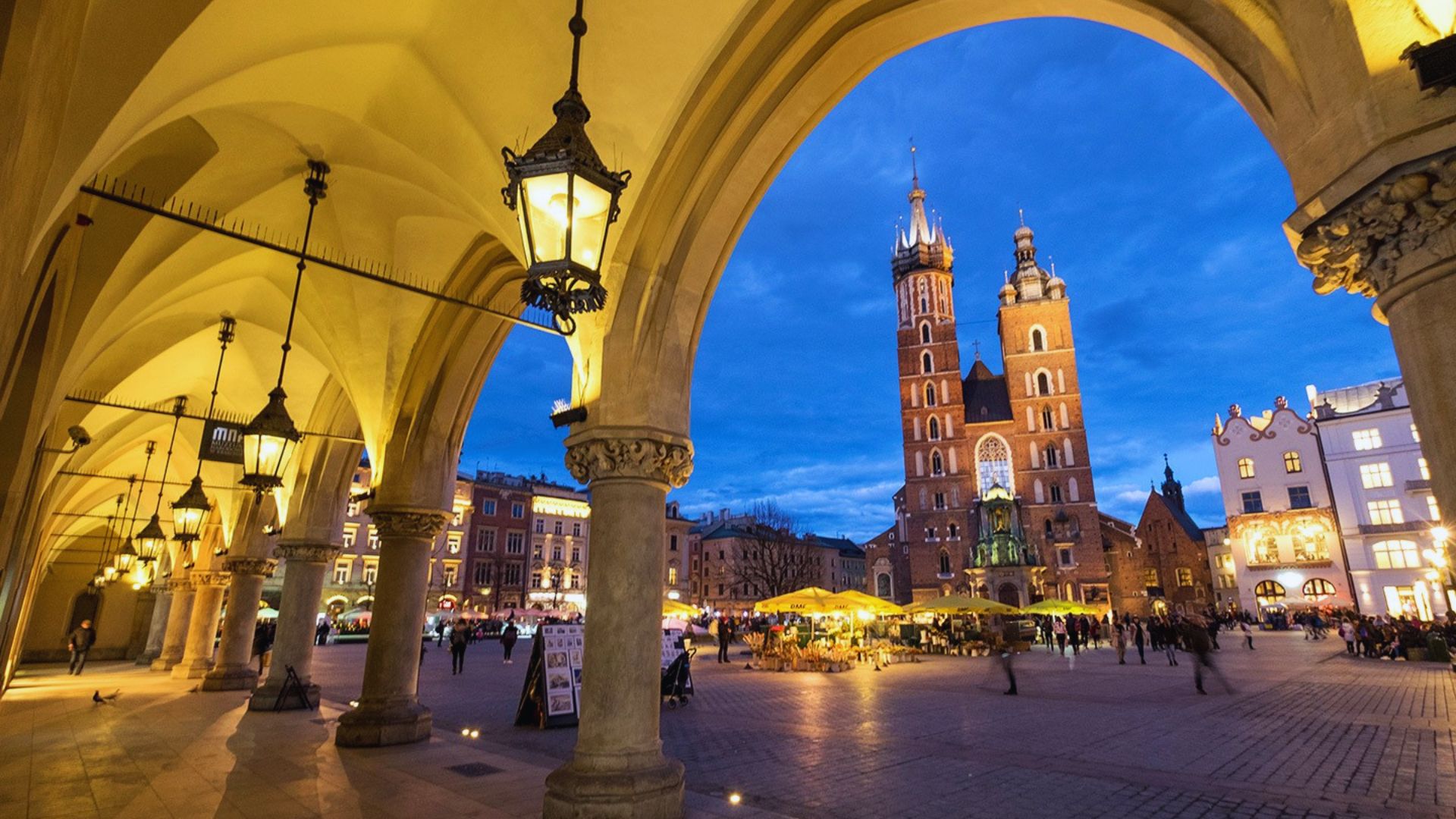 A bustling city square in Krakow, Poland, featuring historic buildings, outdoor cafes, and people enjoying the vibrant atmosphere.