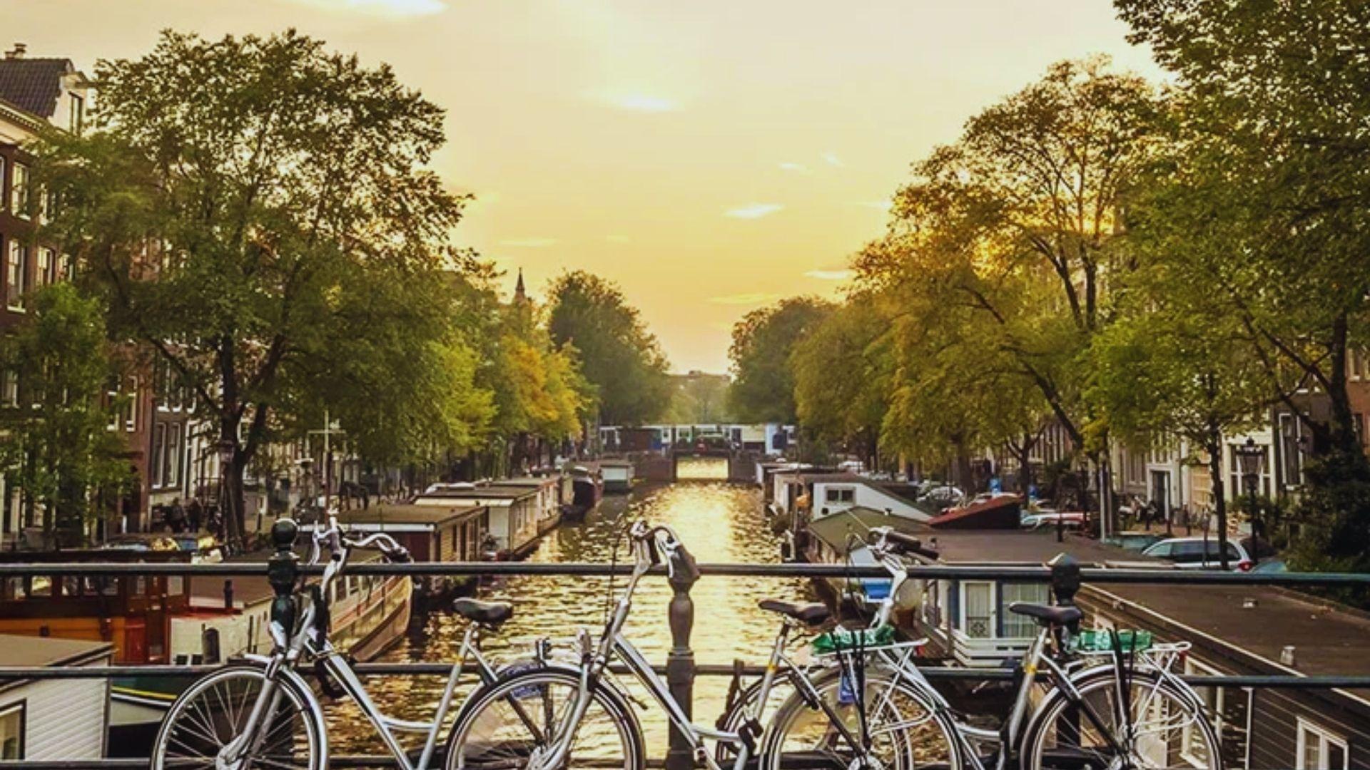 Bicycles are parked on a railing, with a scenic view of a canal in the background.