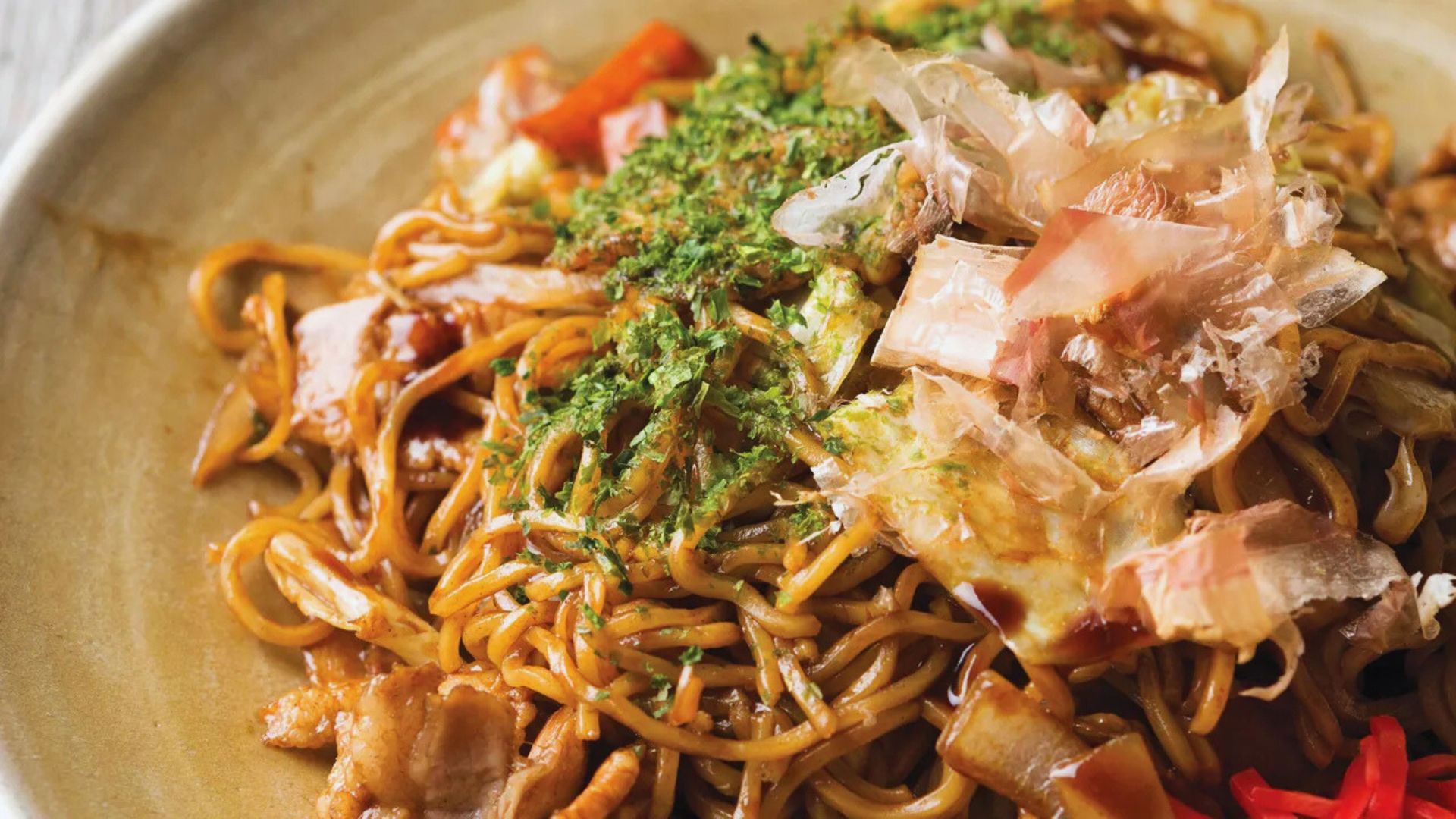 A serving of noodles in a bowl, garnished with tender meat and fresh vegetables, representing a flavorful dish.