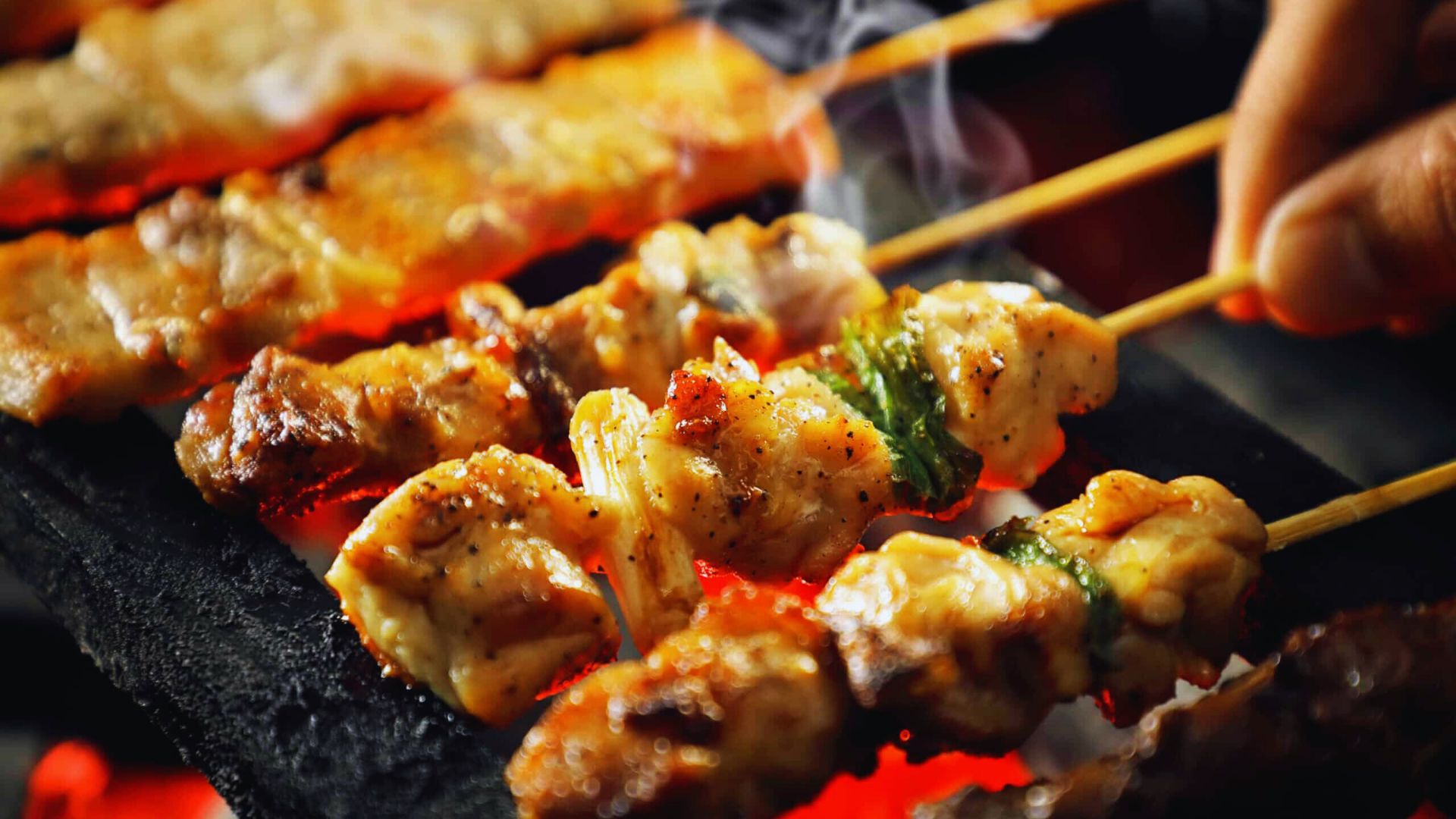 A person grilling skewers over an outdoor grill, showcasing a variety of colorful vegetables and meats.