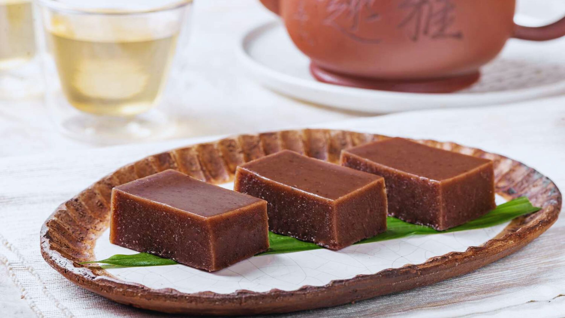 A slice of chocolate cake garnished with green leaves, presented on a white plate.