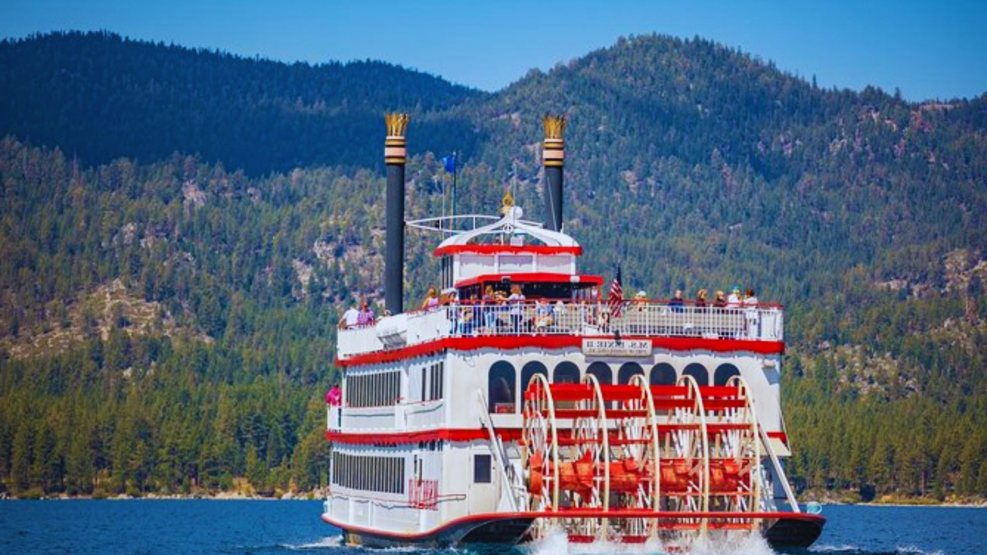 A large white and red paddle boat floating on calm water under a clear sky.