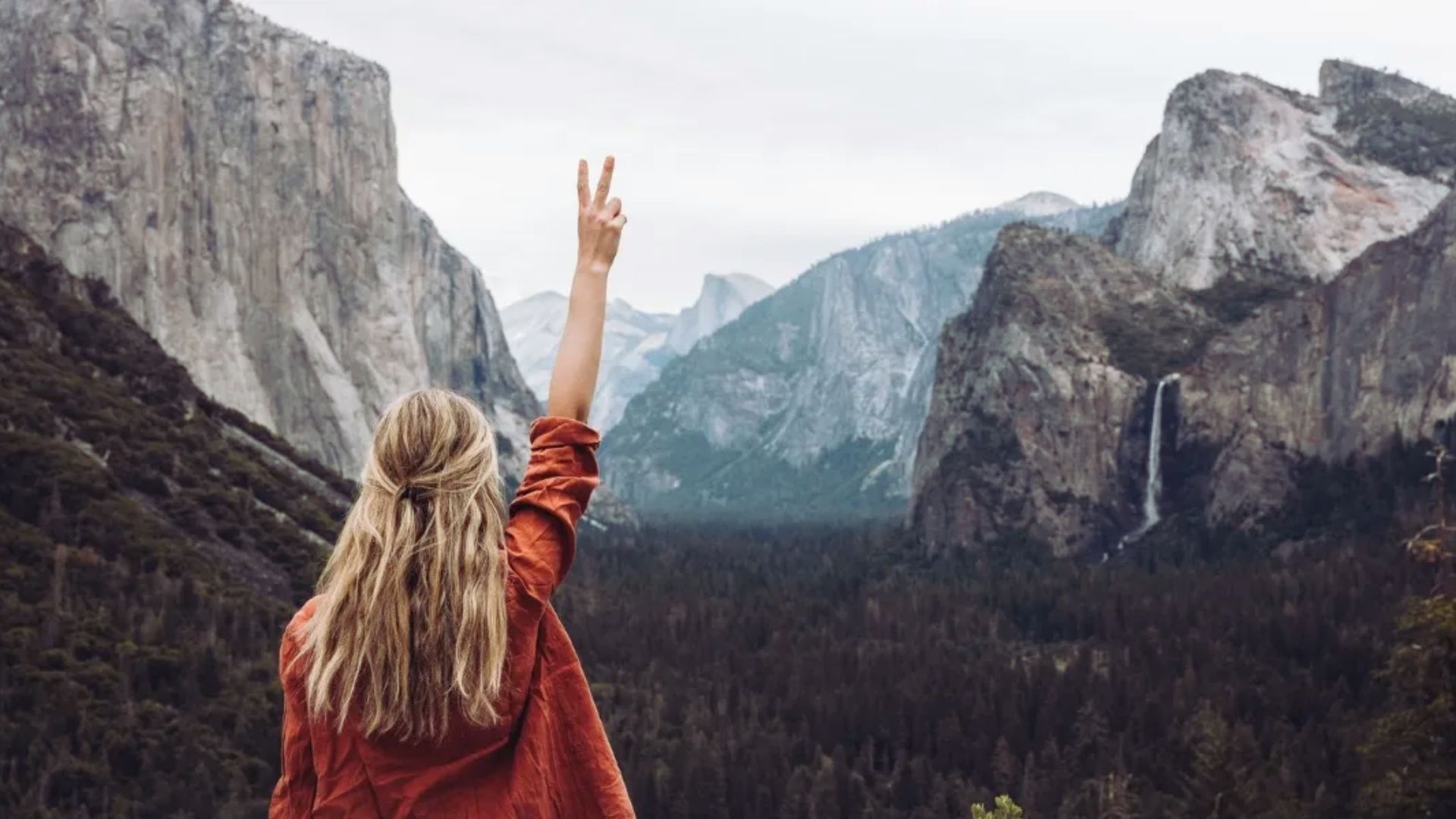 A woman raises her hands in celebration against a backdrop of a majestic mountain.