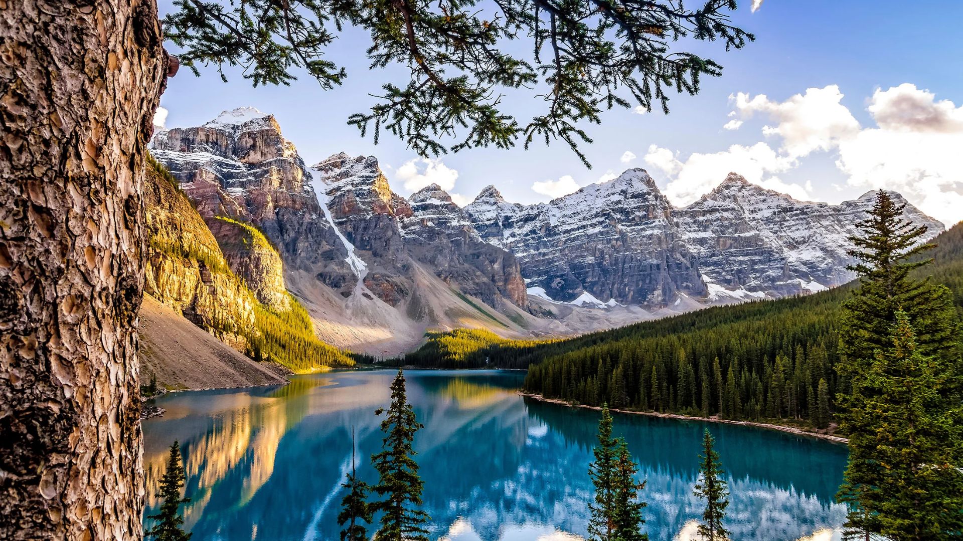 Serene mountain landscape with snow-capped peaks, pine trees, and a clear blue lake reflecting the sky. The scene conveys tranquility and natural beauty.