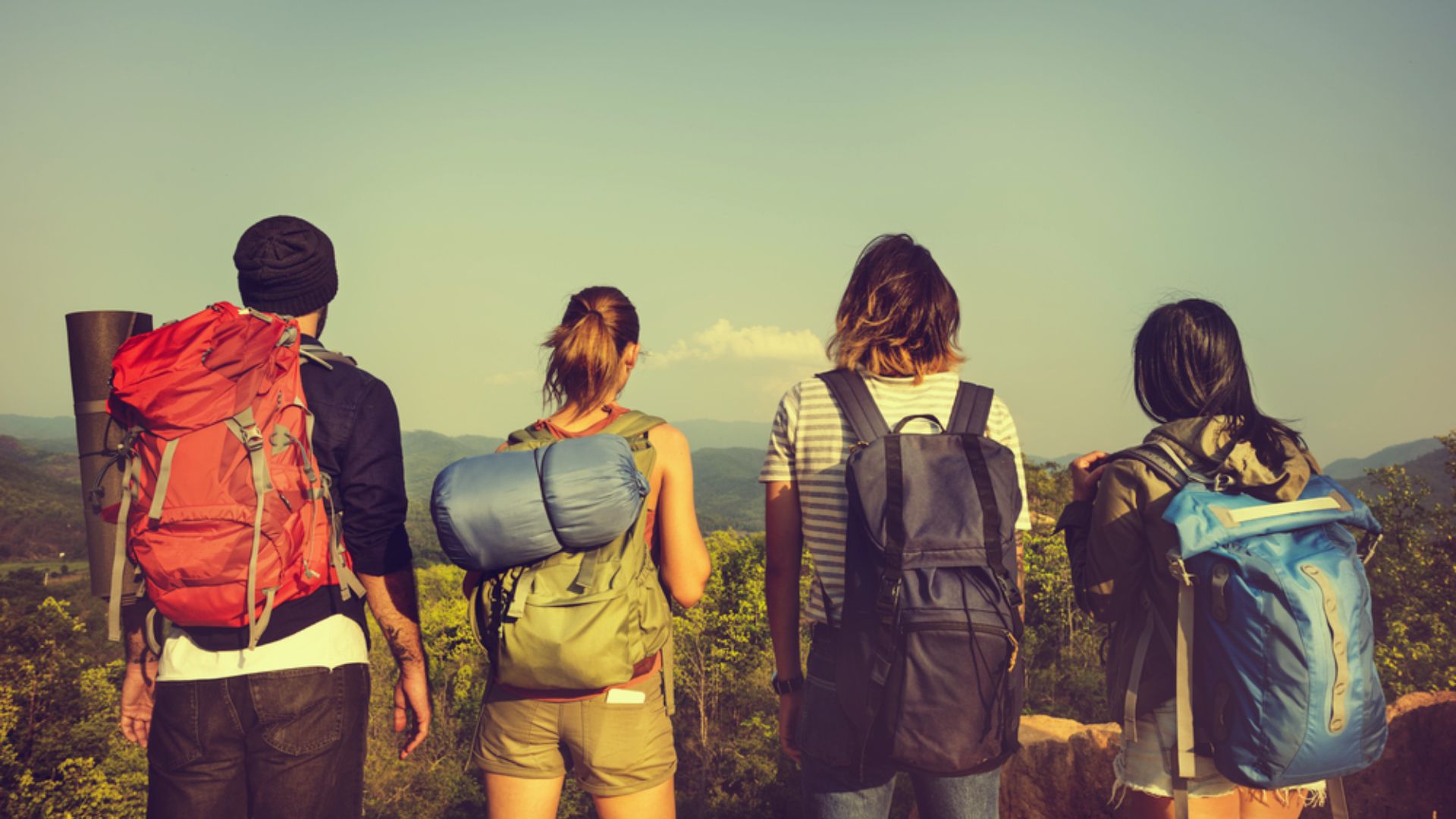 Four individuals with backpacks stand on a hill, enjoying the view and the outdoors.
