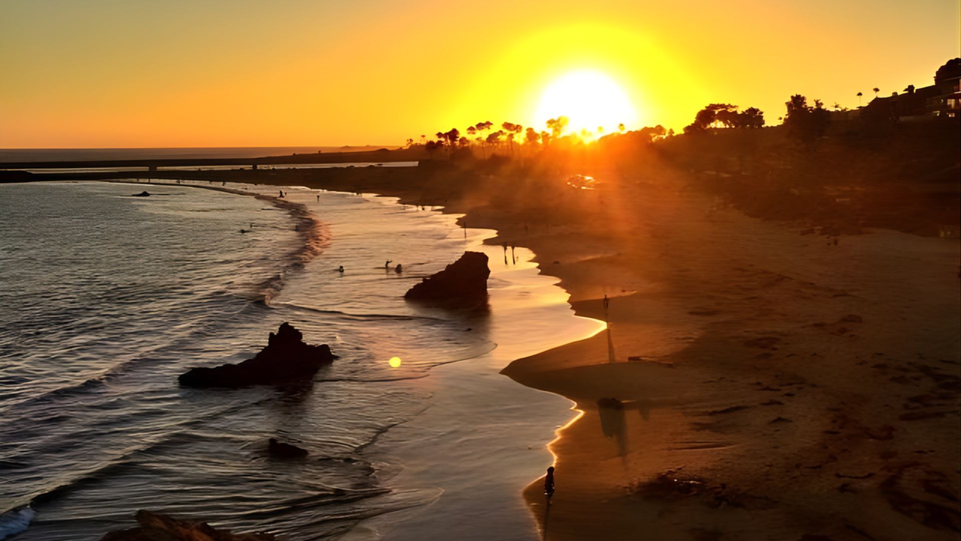 A vibrant sunset casts warm hues over the ocean and beach at Laguna Beach, creating a serene coastal scene.