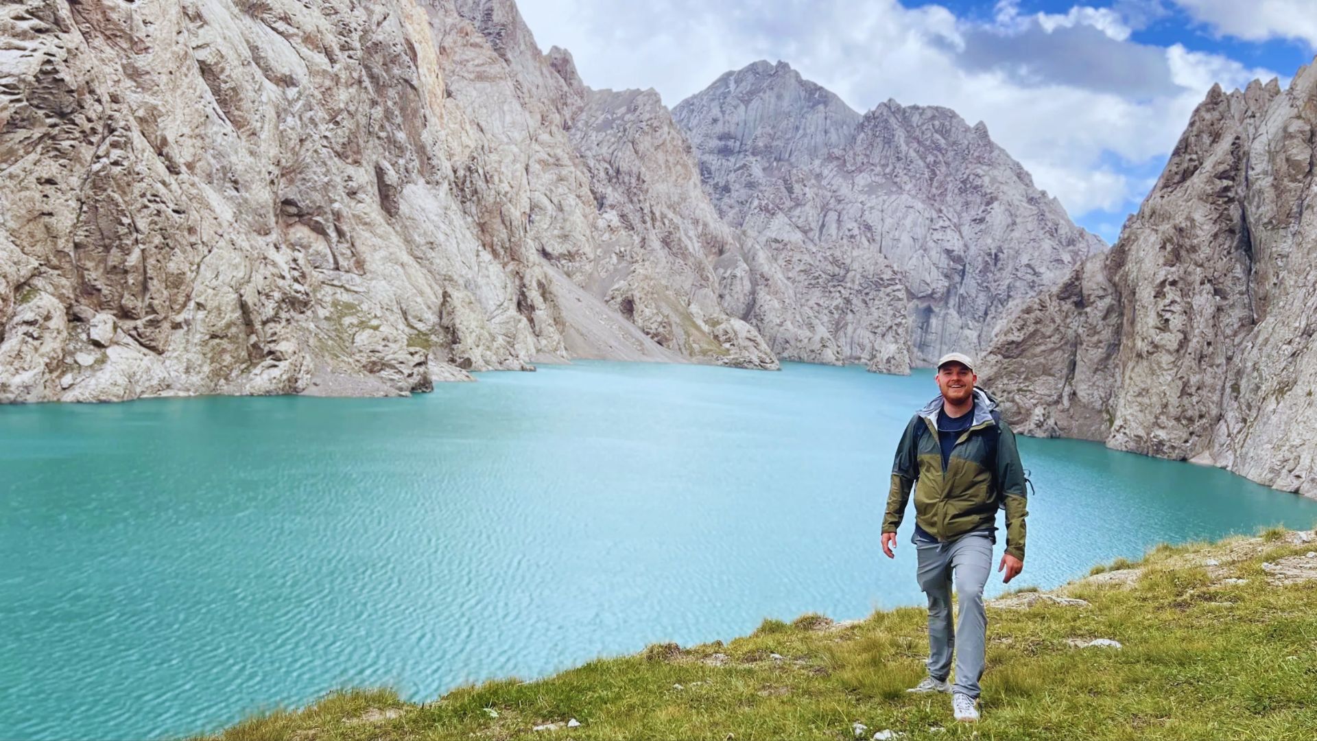 A man stands on a hill, gazing at a serene lake below, surrounded by lush greenery.