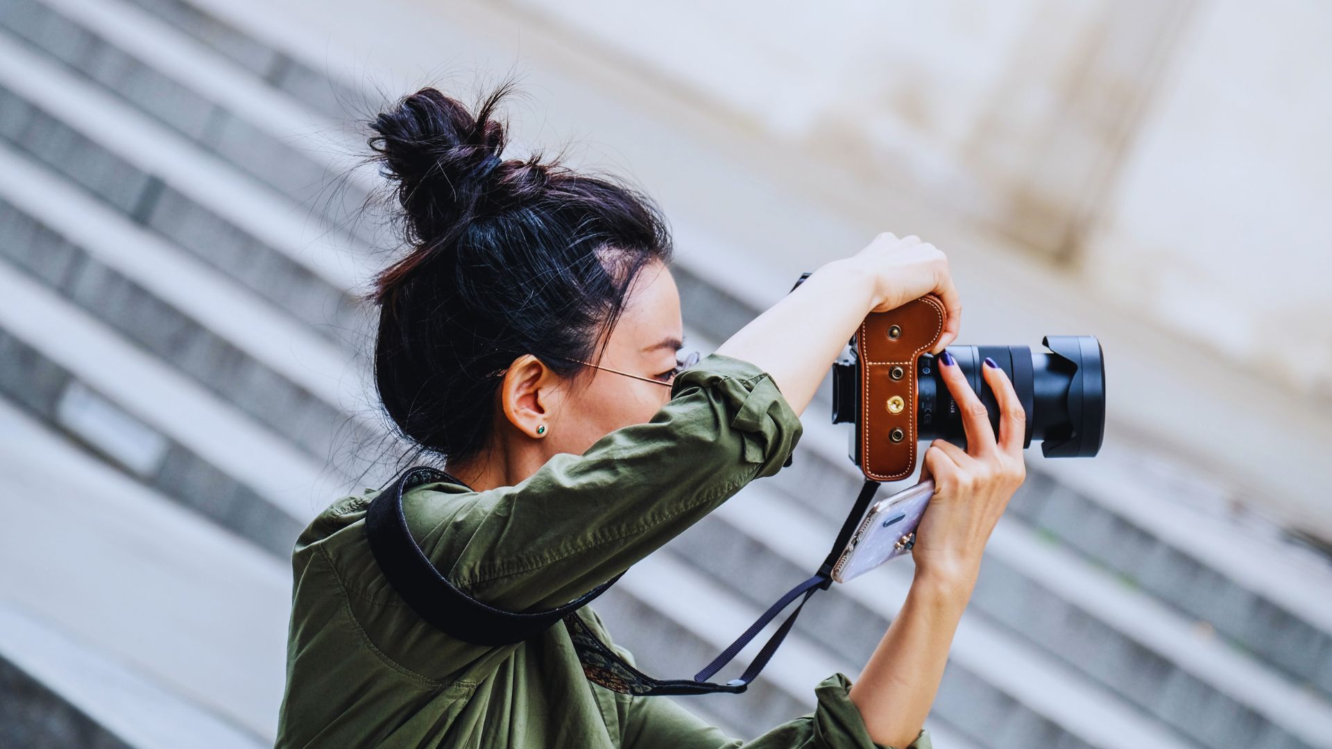 A woman capturing an image with a camera, focused on her subject in an outdoor setting.