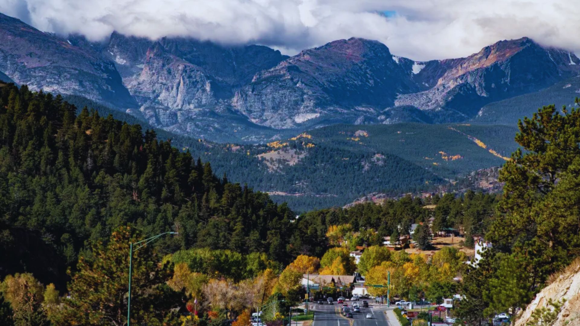 Scenic view of Colorado mountains overlooking a charming town, showcasing lush greenery and clear blue skies.