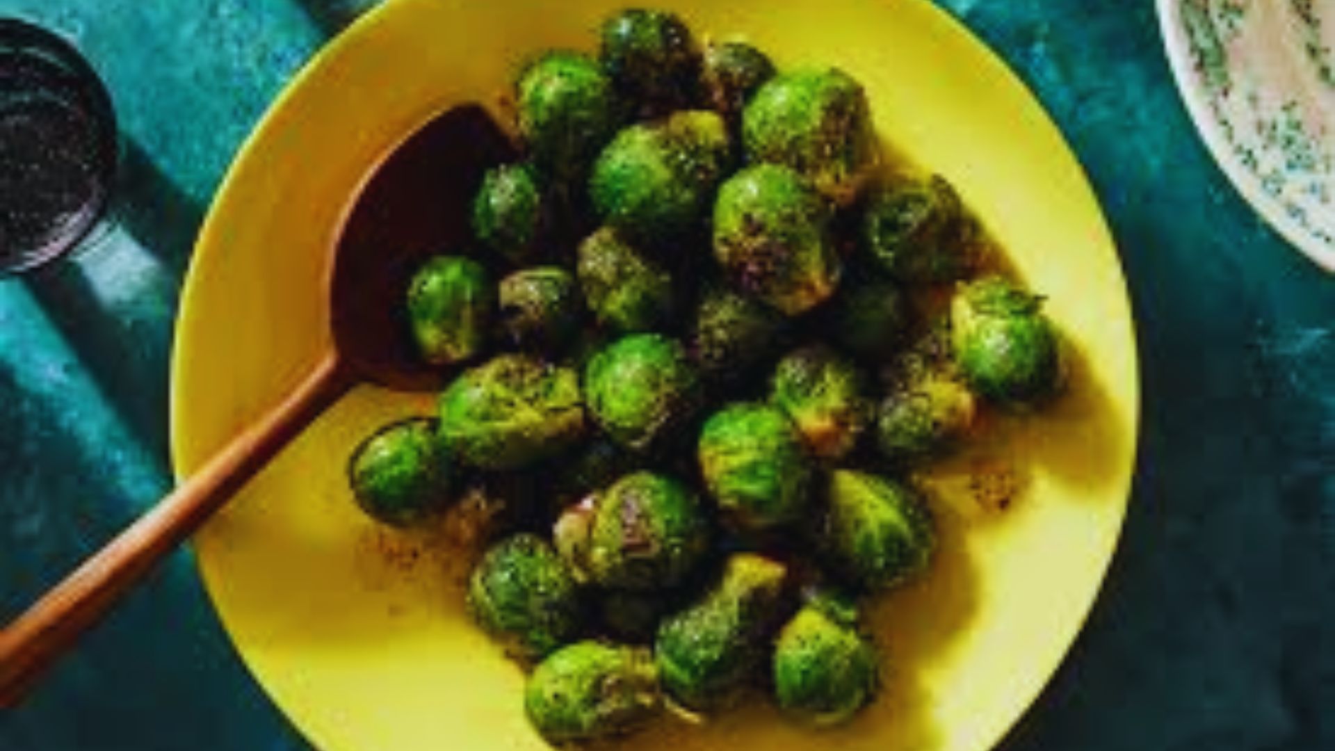 A plate of cooked brussels sprouts accompanied by a wooden spoon, ready to be served.