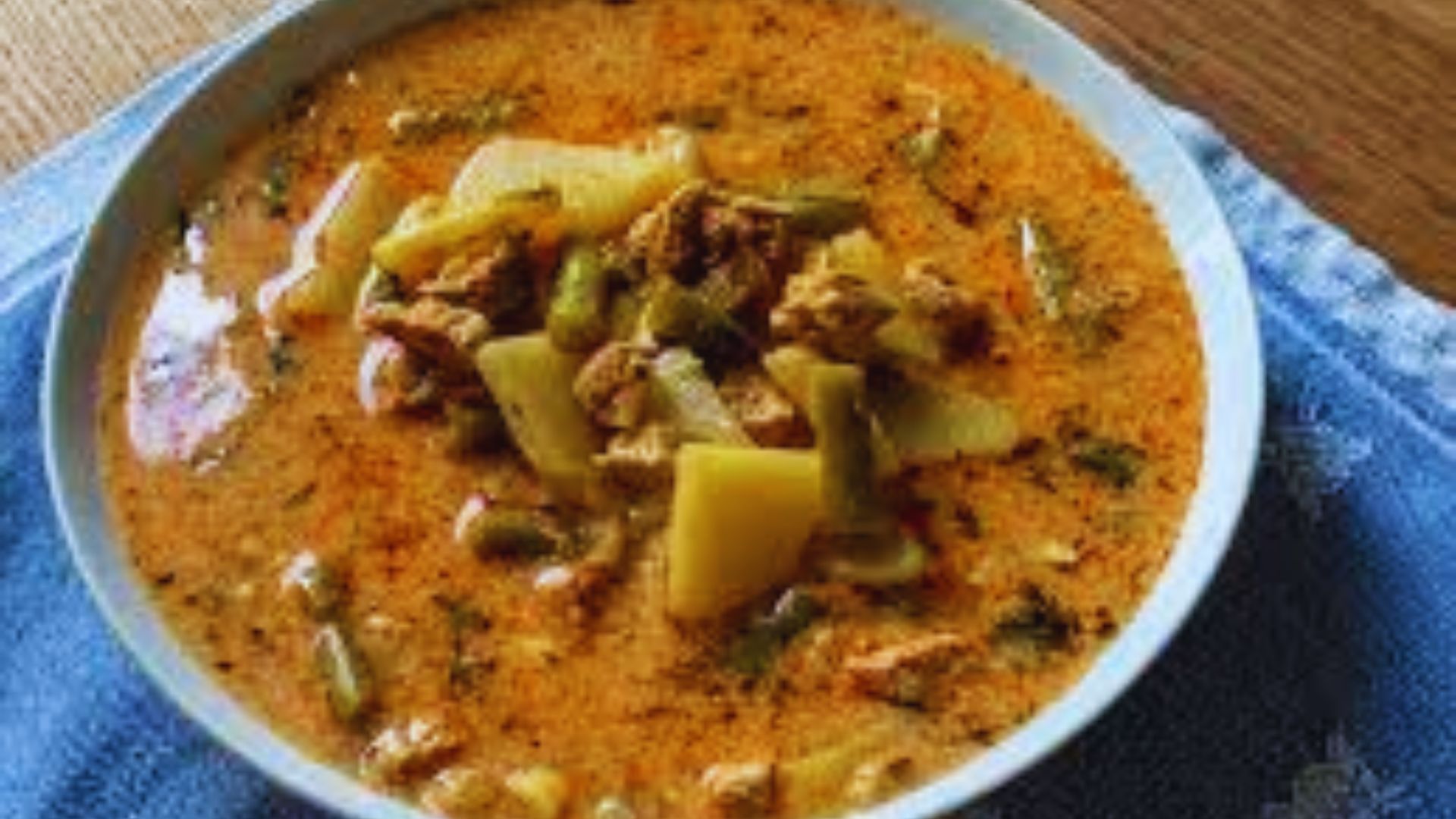 A bowl filled with meat and vegetable soup, resting on a blue napkin.