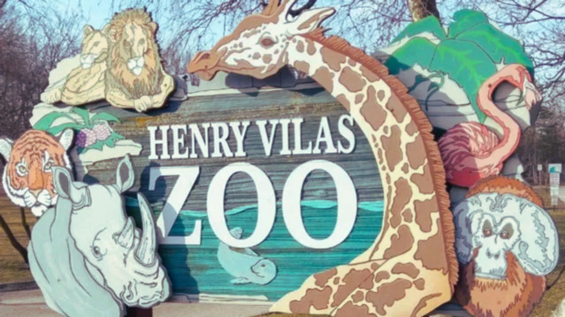 Sign for Henry Vilas Zoo featuring illustrations of animals, including a giraffe, rhinoceros, lion, and flamingo, creating a welcoming and vibrant tone.