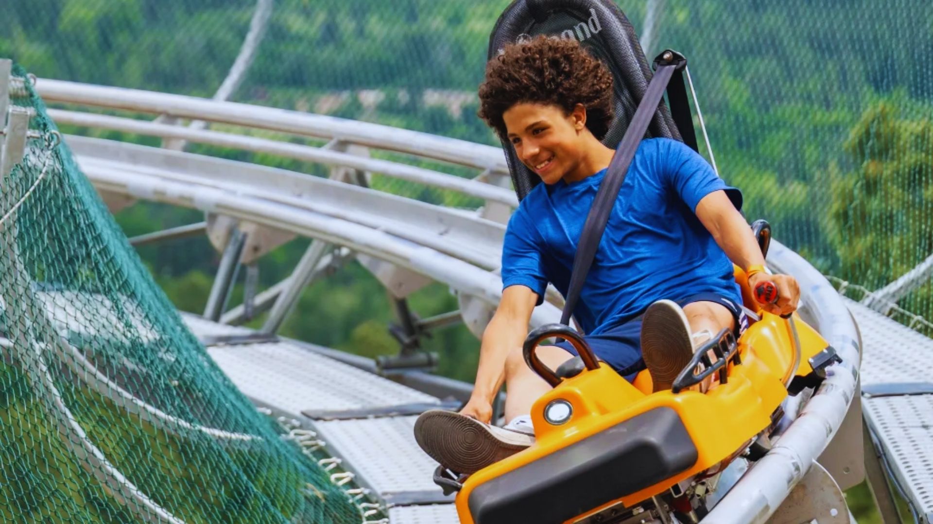 A young man joyfully riding a roller coaster, with his hands raised and a big smile on his face.