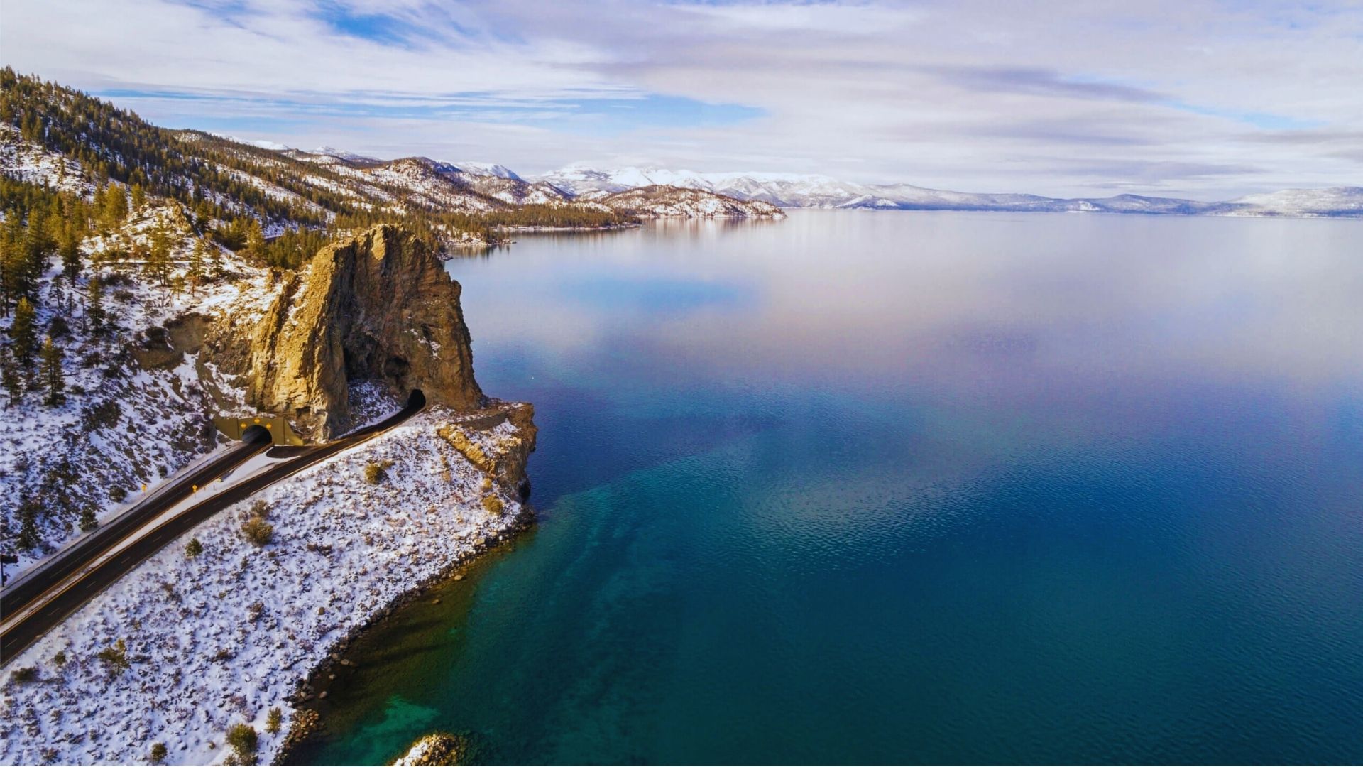 Aerial view showcasing a serene lake surrounded by majestic mountains under a clear blue sky.