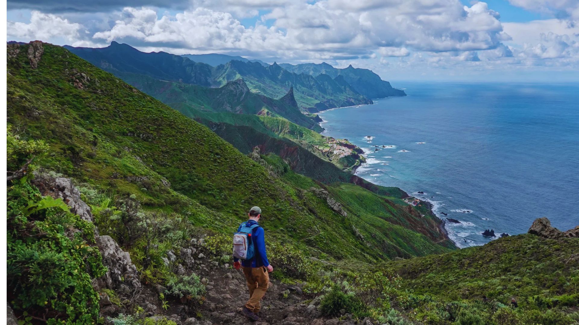 A man ascends a steep hill, overlooking the ocean in the distance.