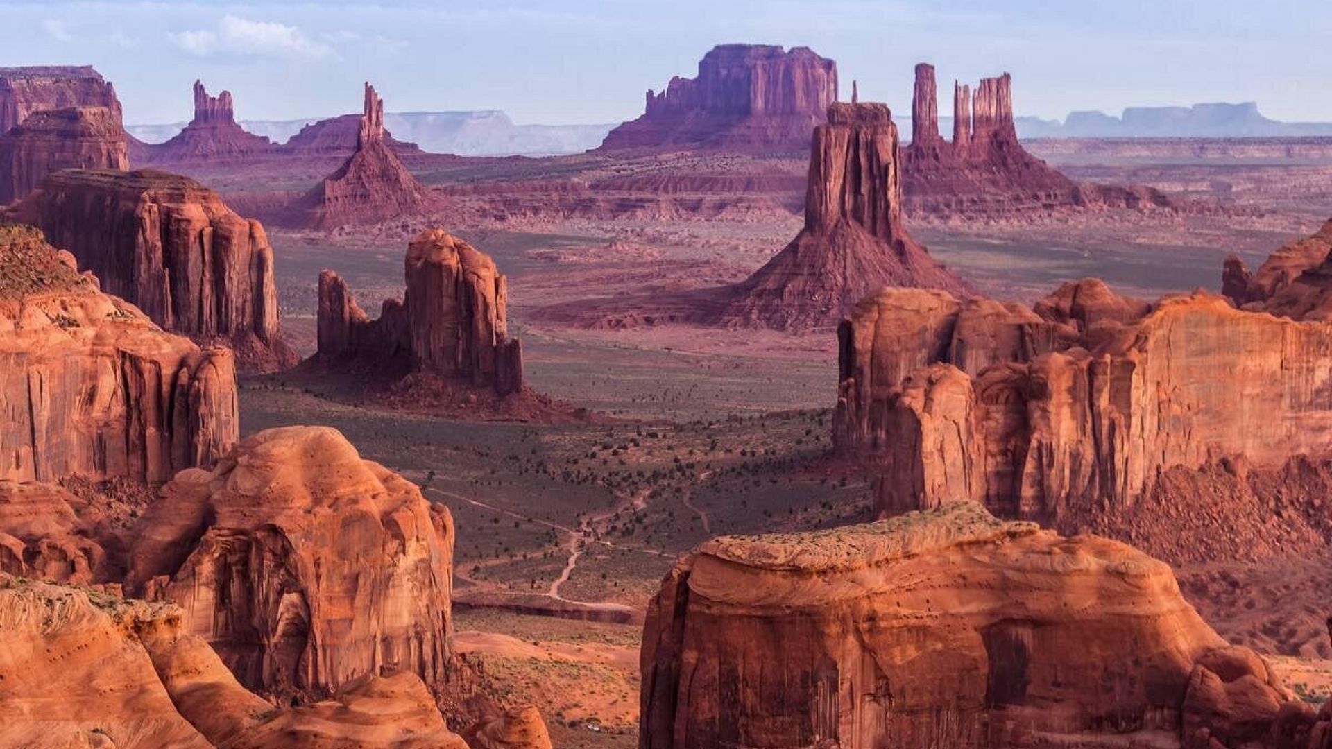 Monument Valley features vast desert landscapes with striking red rock formations under a clear blue sky.