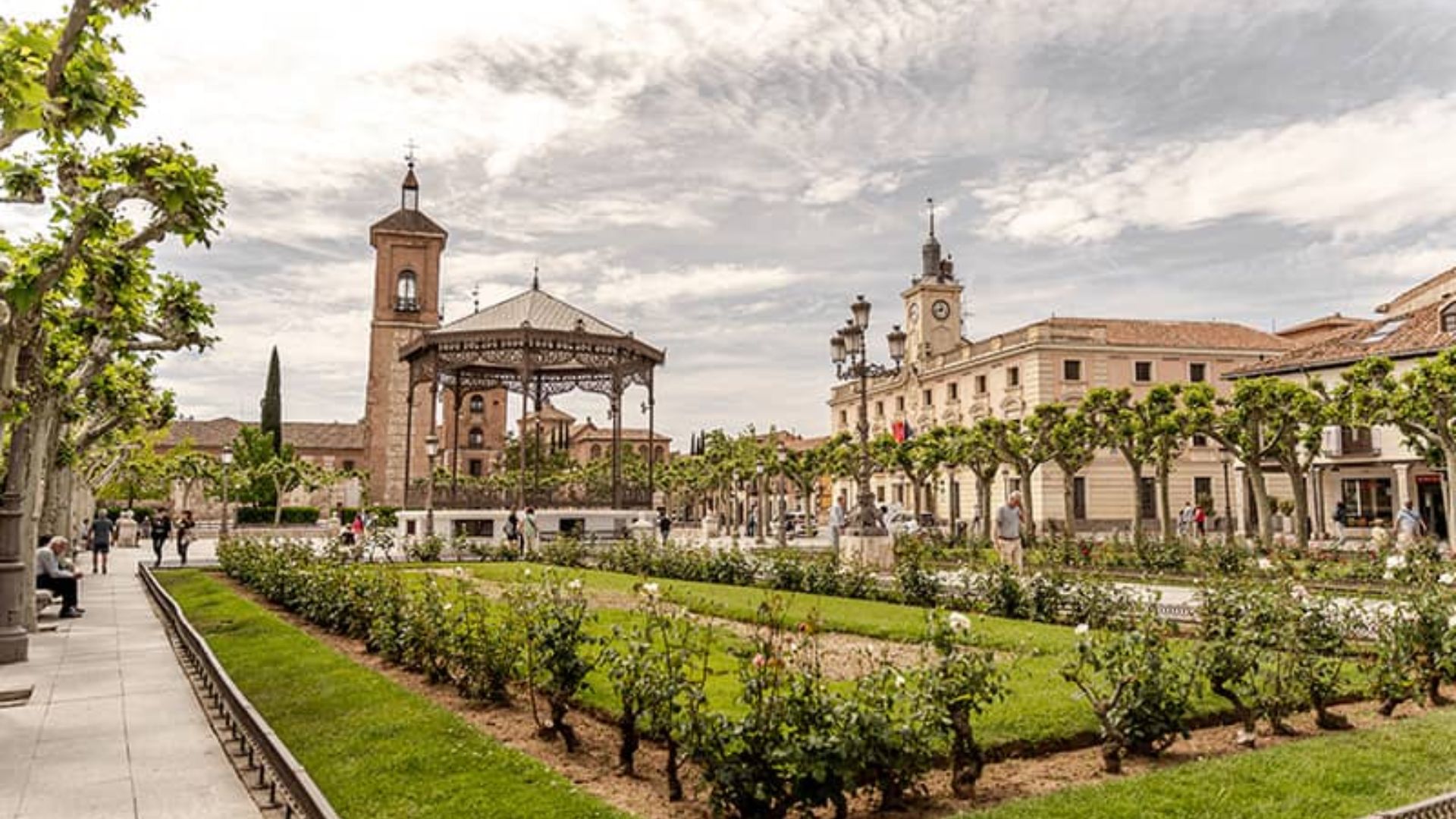 A city square featuring a prominent clock tower surrounded by a vibrant garden.