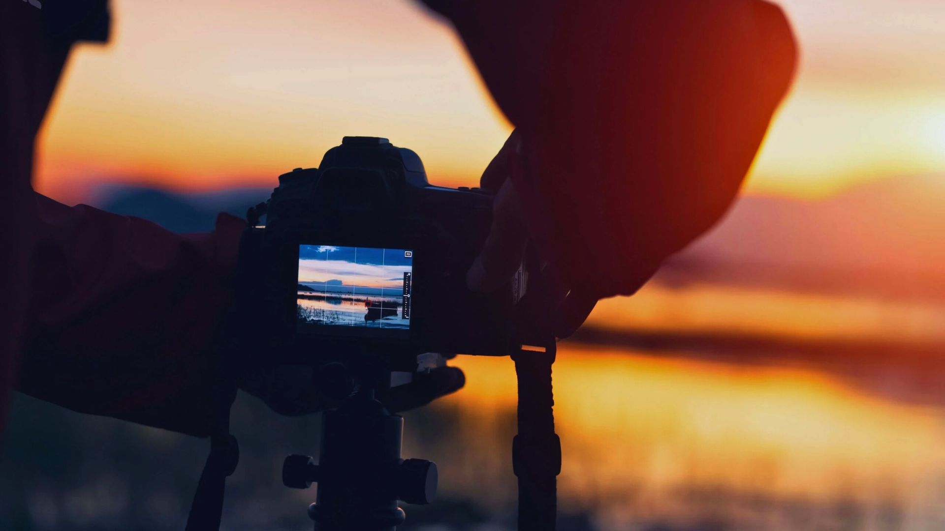 Individual capturing a sunset with a camera, surrounded by warm hues of orange and pink.