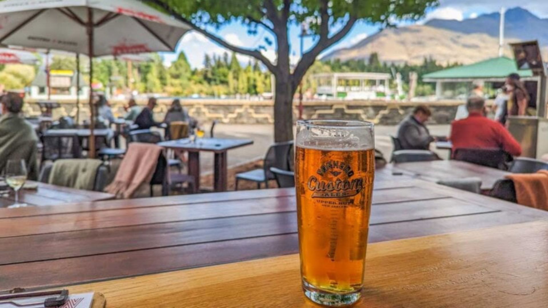 A beer glass sits on a table, with a scenic mountain backdrop in the distance.