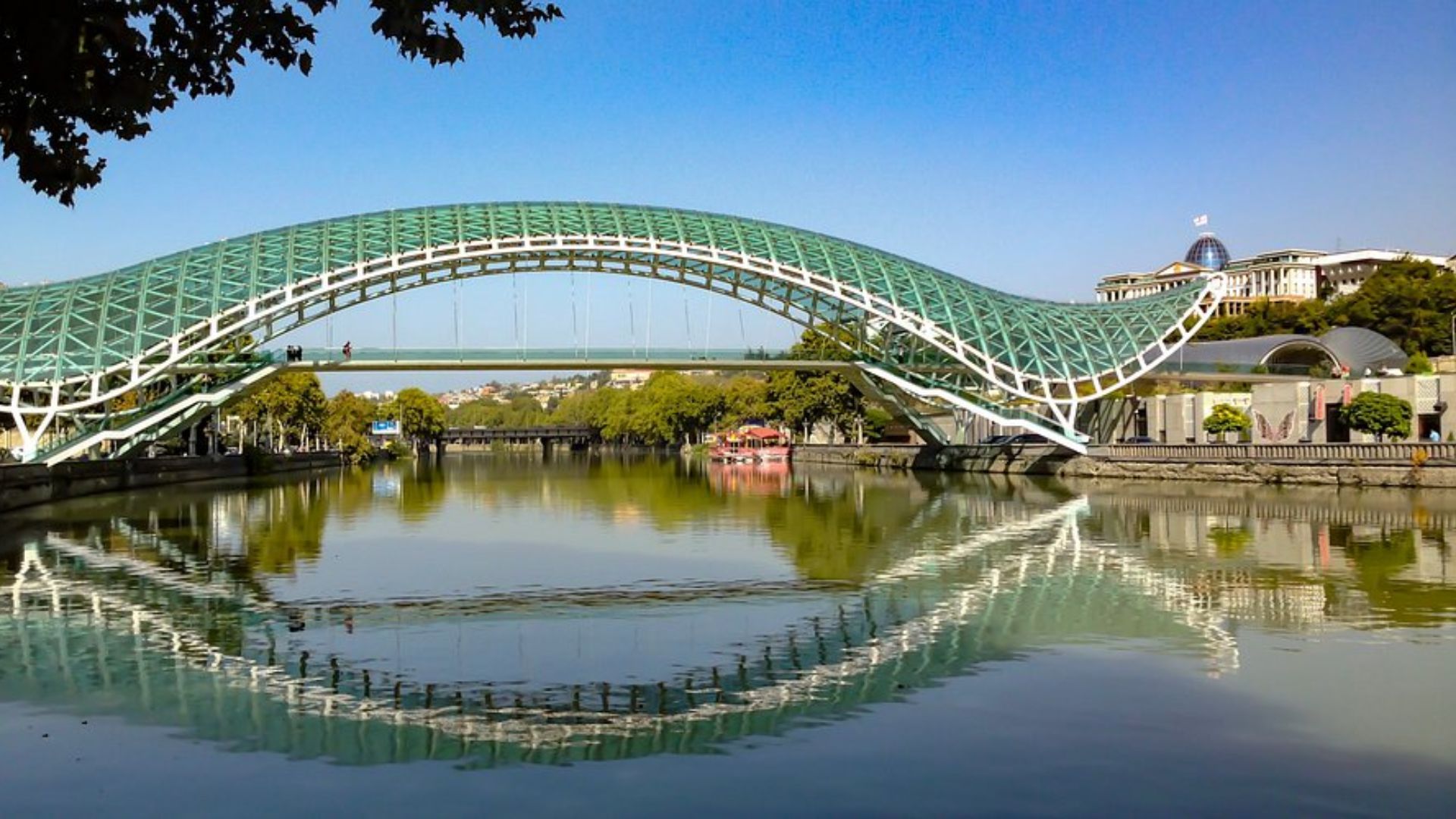 A green-arched bridge spans a river, surrounded by lush greenery and reflecting the serene landscape.