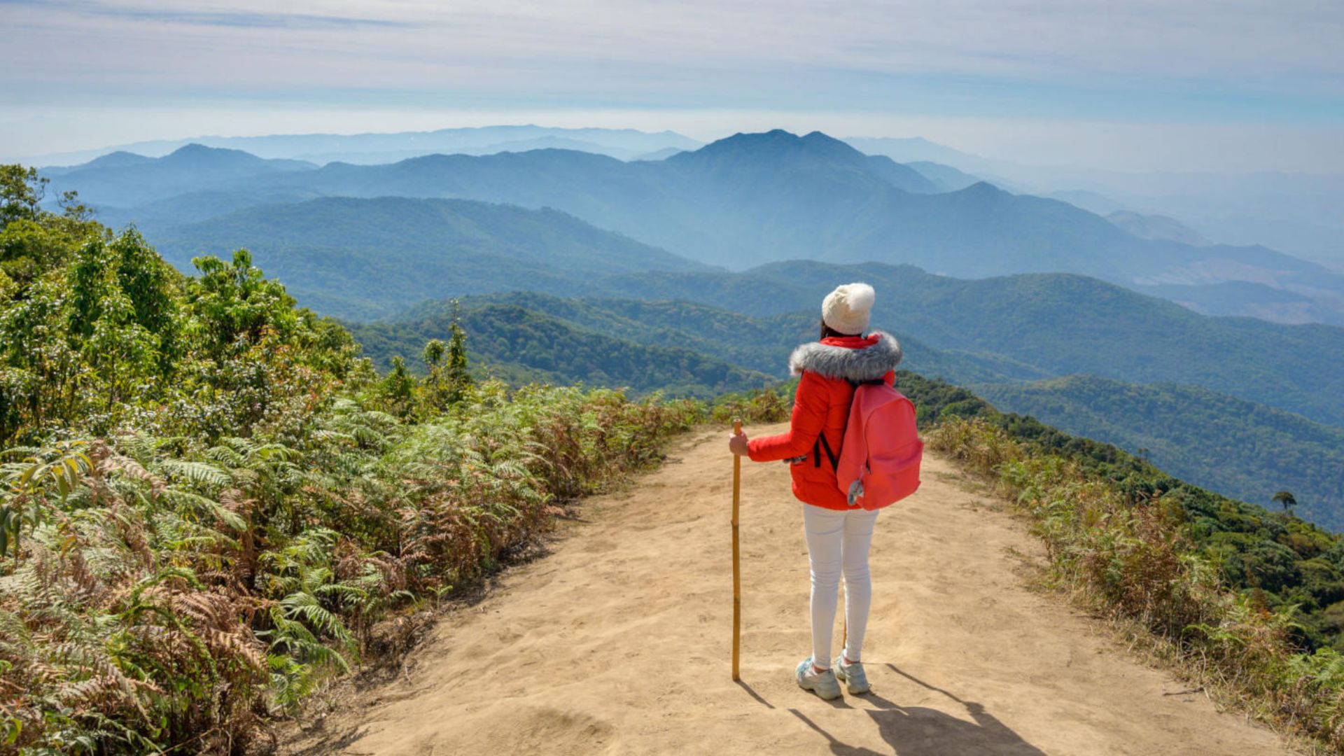 A woman equipped with a backpack and hiking poles navigates a trail, enjoying the outdoors and nature around her.