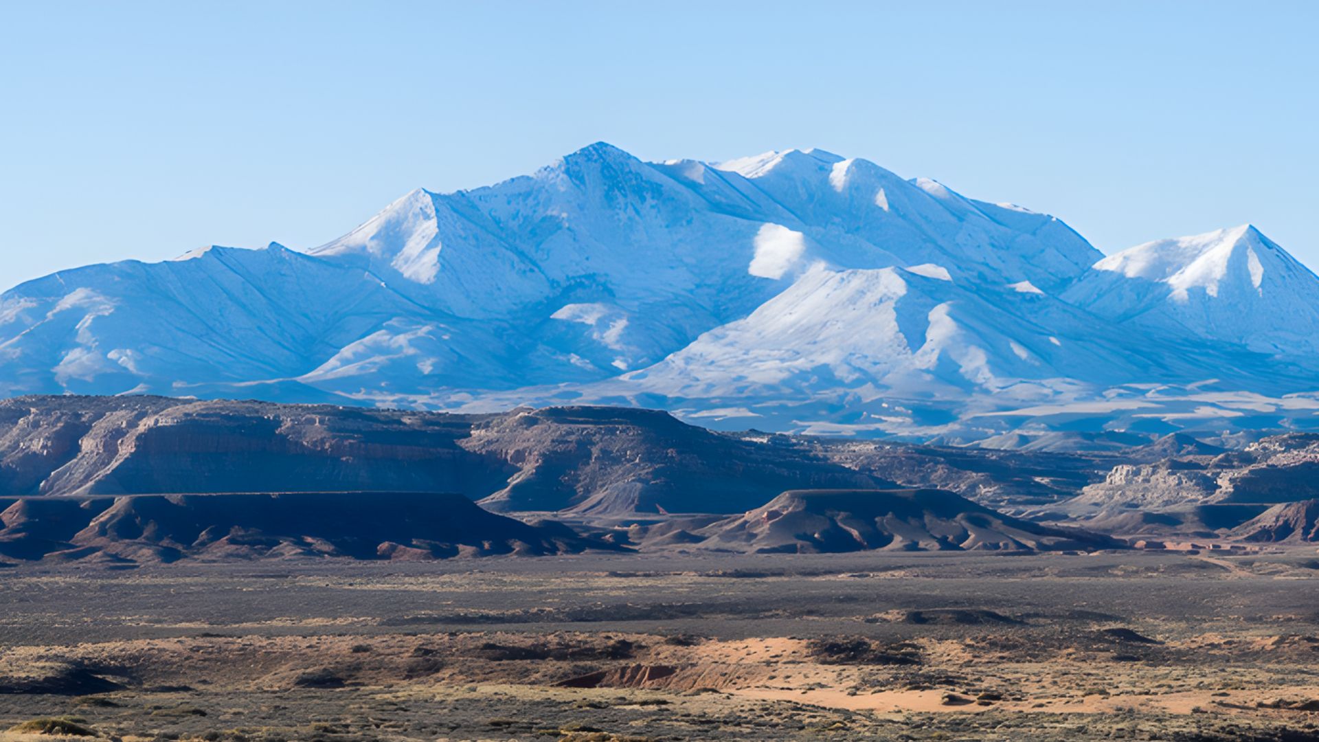 A panoramic view of a majestic mountain range under a clear blue sky, showcasing rugged peaks and lush valleys.