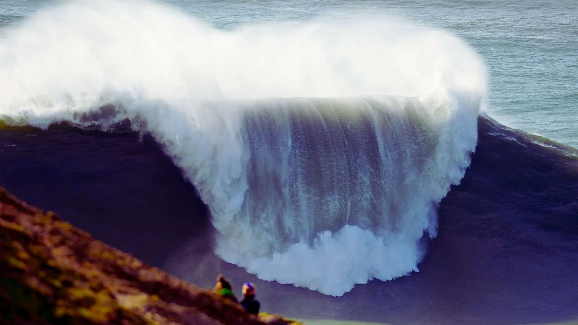 A large wave crashes dramatically into the ocean, creating a splash and showcasing the power of nature.