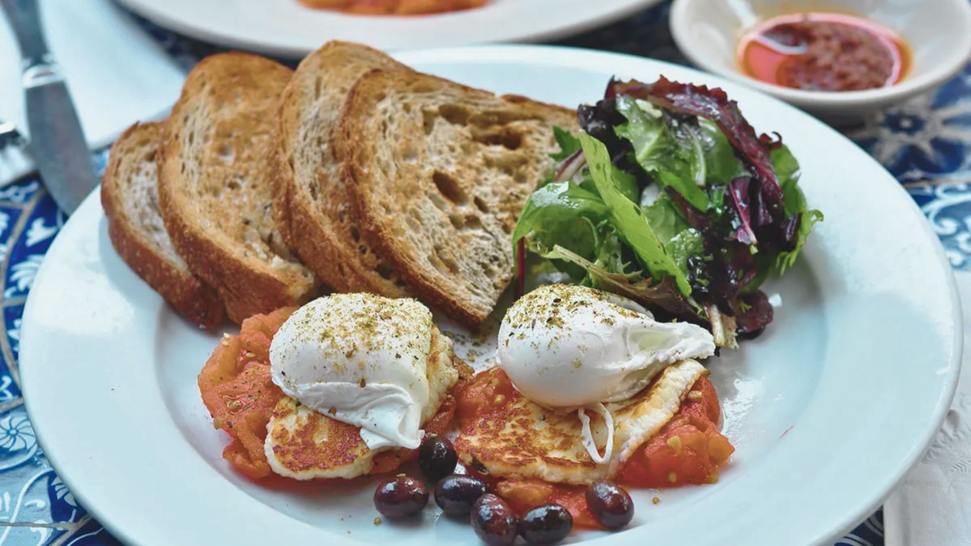 A dish containing poached eggs, whole grain bread, and a colorful salad mix.