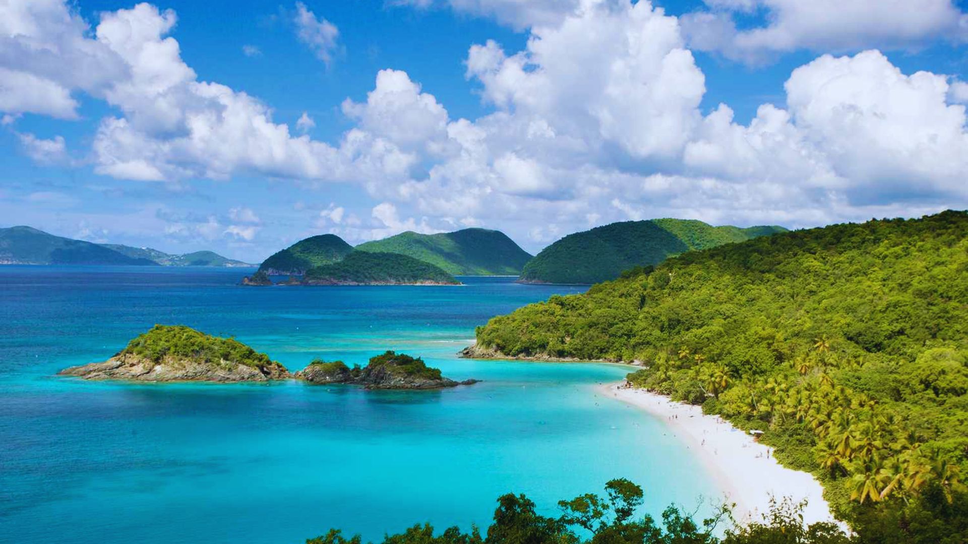 A serene tropical beach with turquoise waters, lush green hills, and a clear blue sky with fluffy clouds, conveying a peaceful and inviting atmosphere.