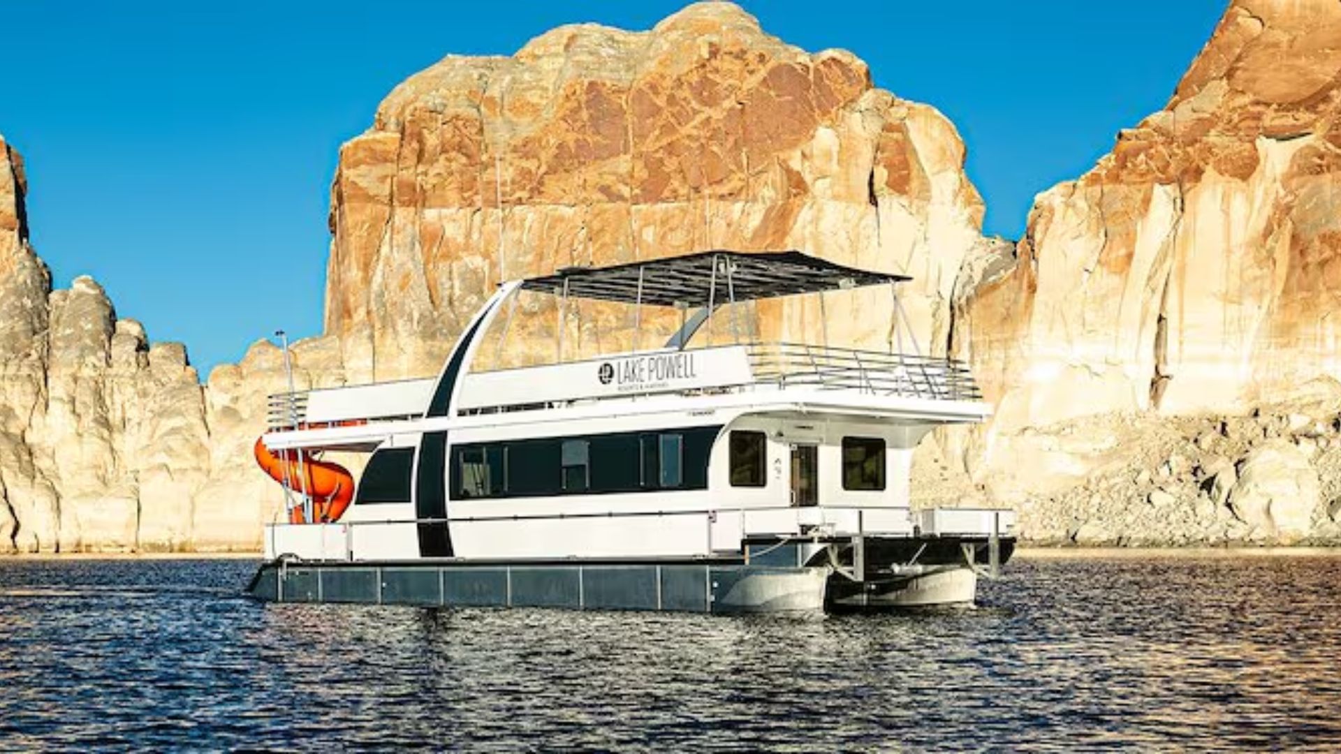 A houseboat floats on the water near rocky formations, surrounded by a serene natural landscape.