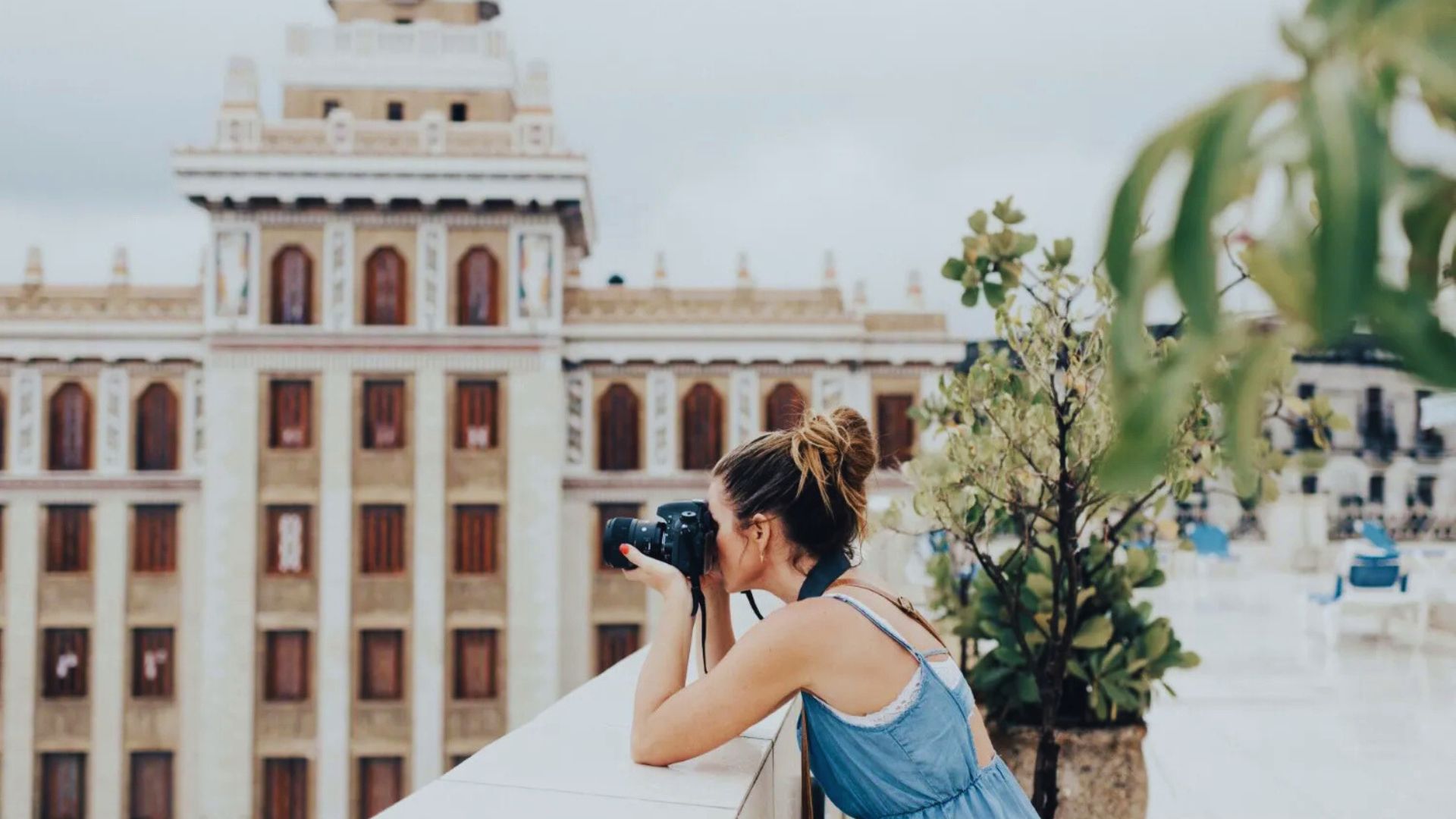 A woman photographing a tall building with a camera, capturing its architectural details against a clear sky.