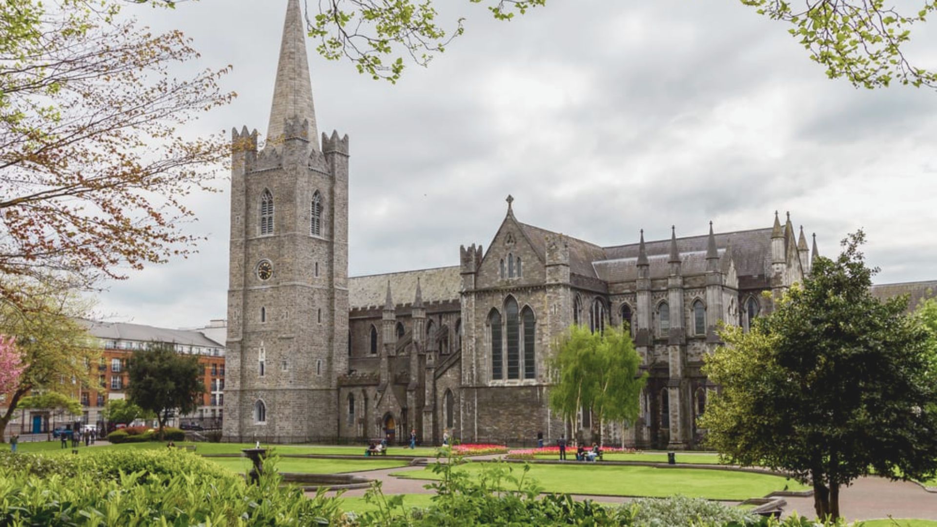 A majestic cathedral with a tall steeple is surrounded by a lush green field, creating a serene landscape.