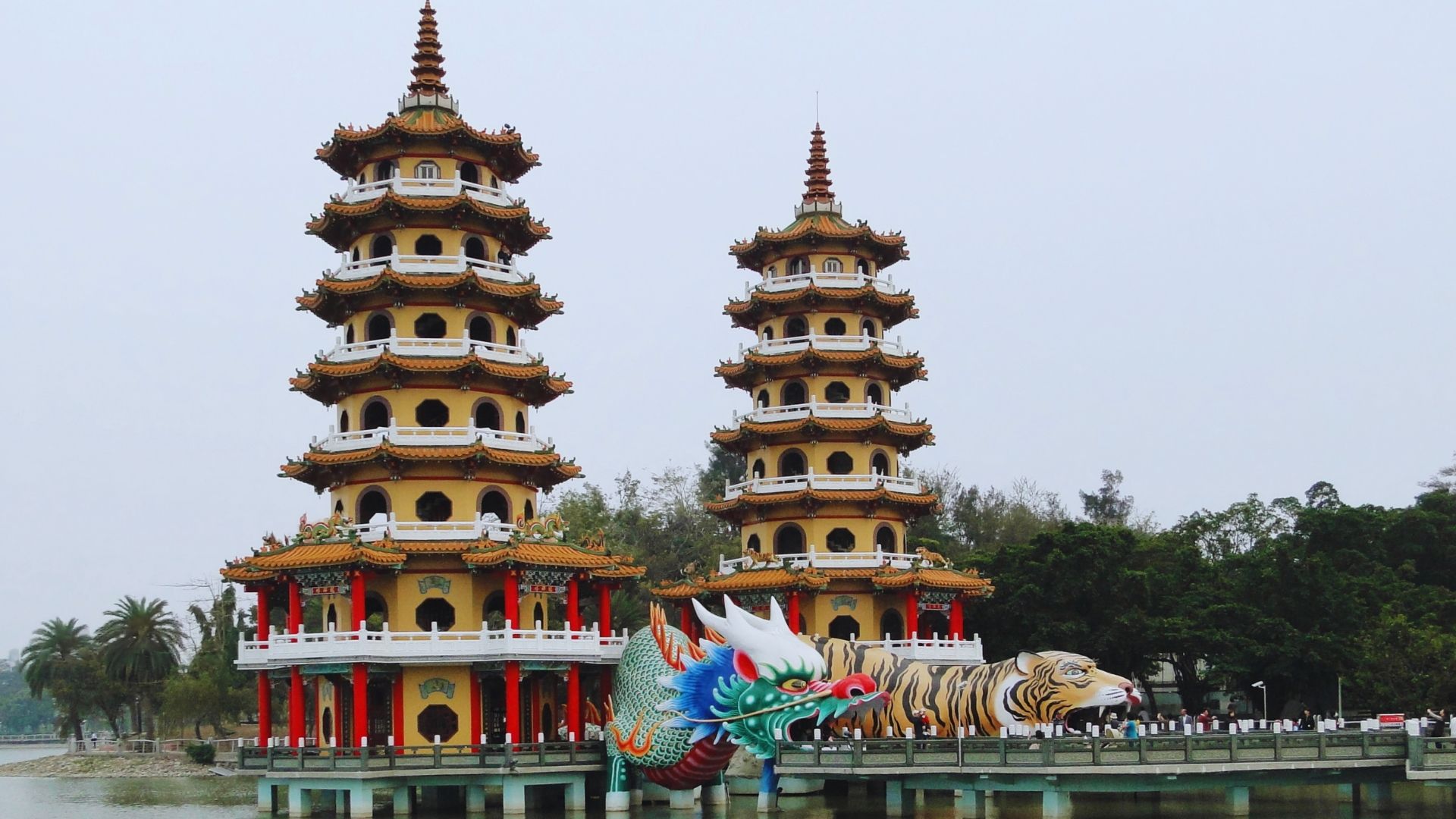 Two ornate pagodas with traditional tiered roofs stand by a lake. A colorful dragon and tiger sculpture adorns the entrance, creating a majestic scene.
