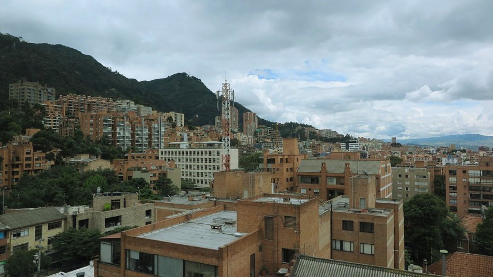 A panoramic view of a Colombian city skyline from a rooftop, showcasing buildings and distant mountains under a clear sky.
