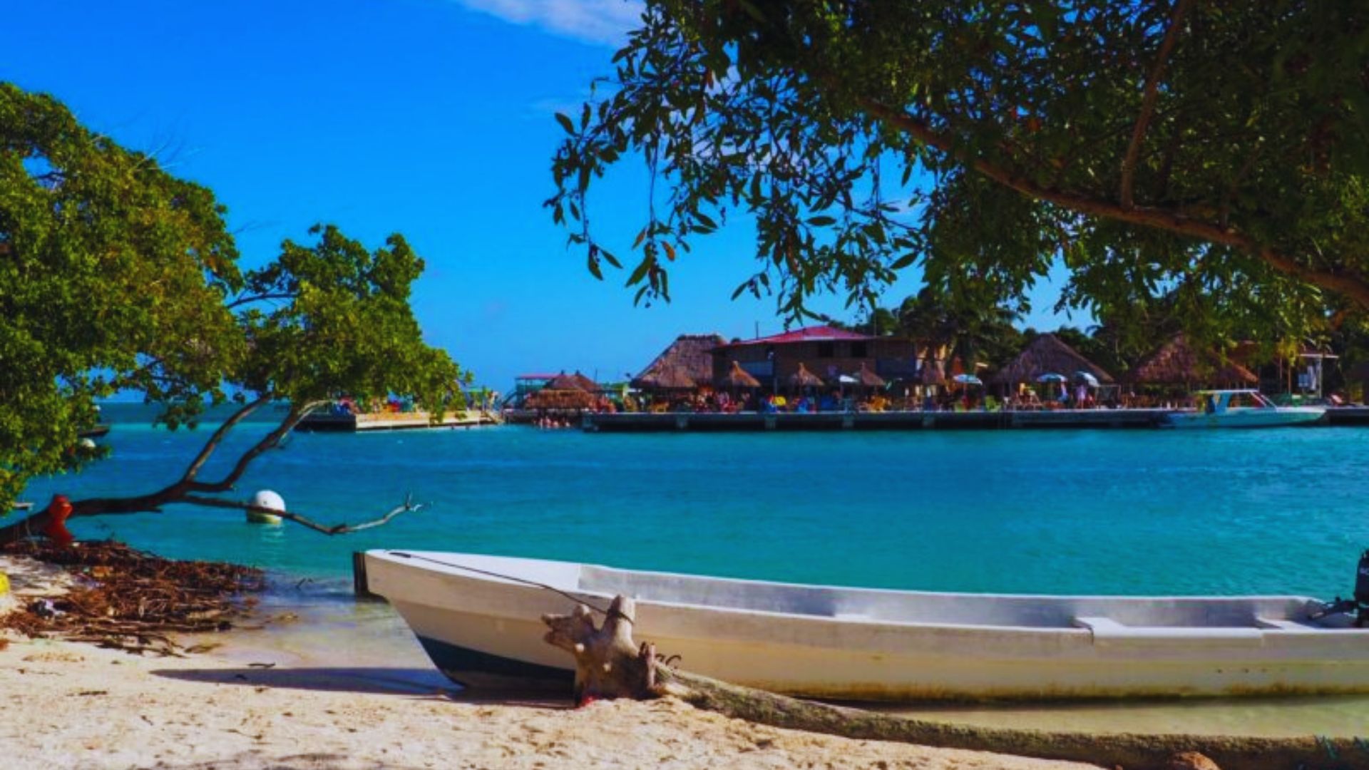 A boat rests on the sandy shore of a beach, with gentle waves lapping at its hull under a clear blue sky.