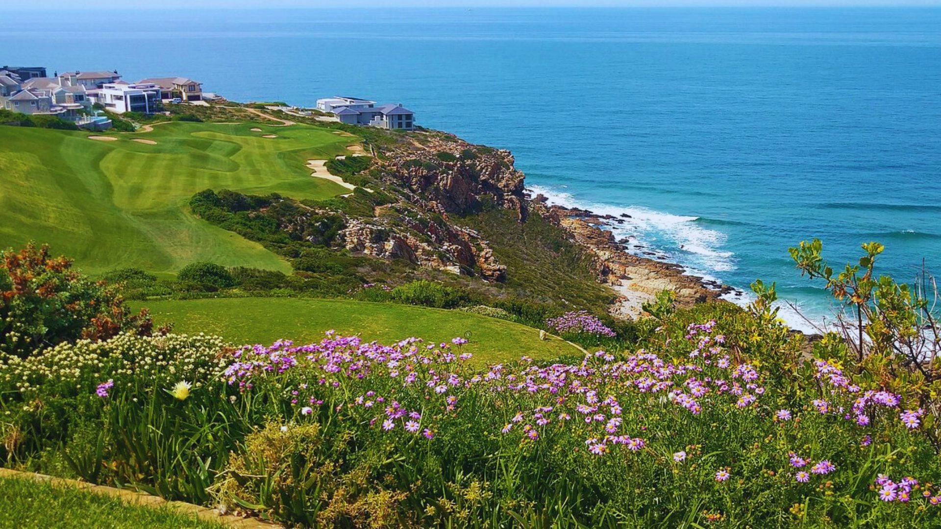 Scenic view of the Cape Town golf course, featuring lush greens and mountainous backdrop under a clear blue sky.
