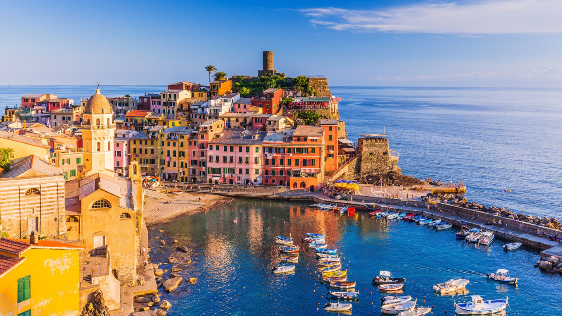 Colorful buildings line the waterfront, with boats gently bobbing in the water under a clear blue sky.