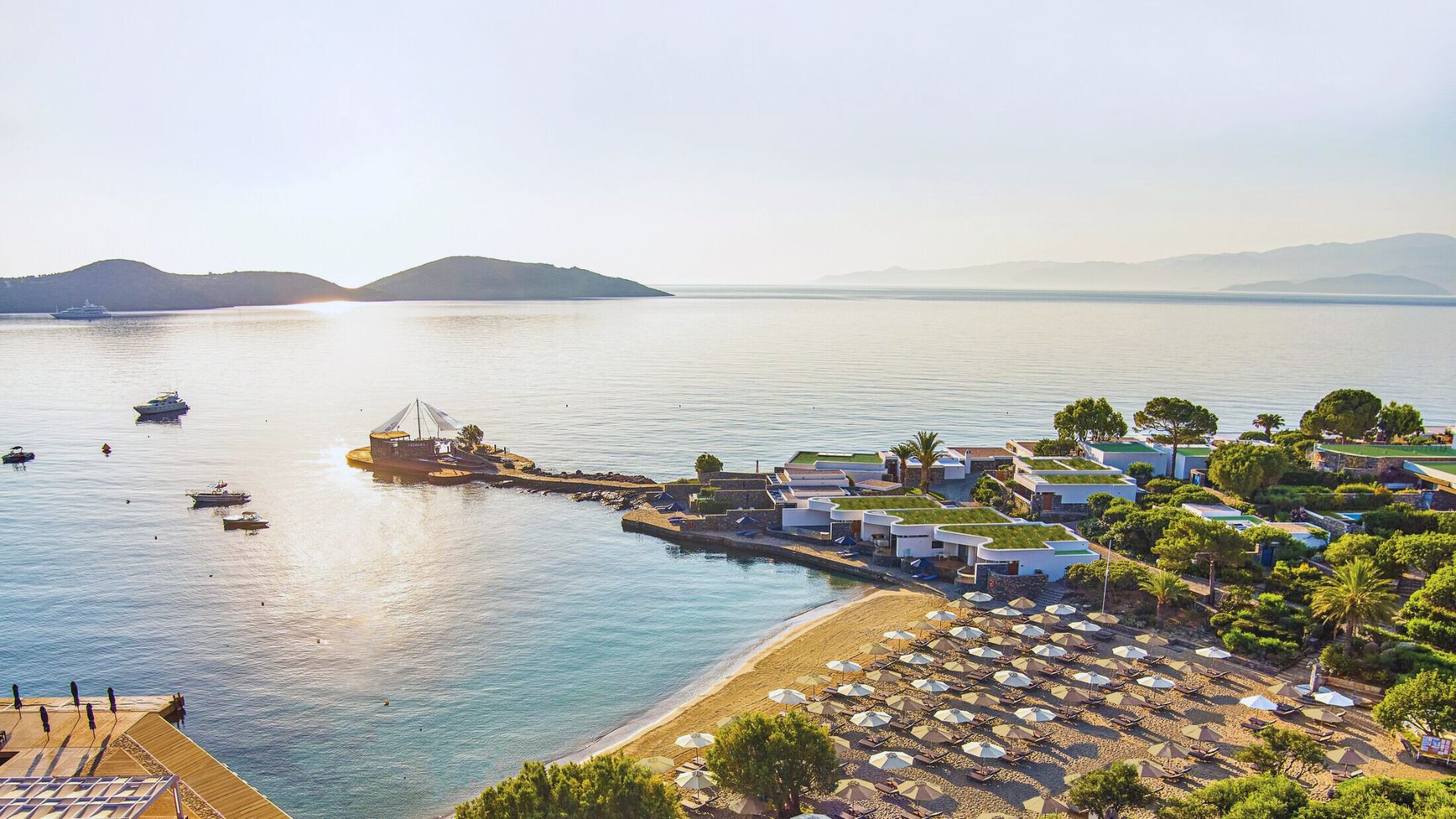 Aerial view of a beach and resort, showcasing sandy shores, turquoise waters, and palm trees in a tropical setting.