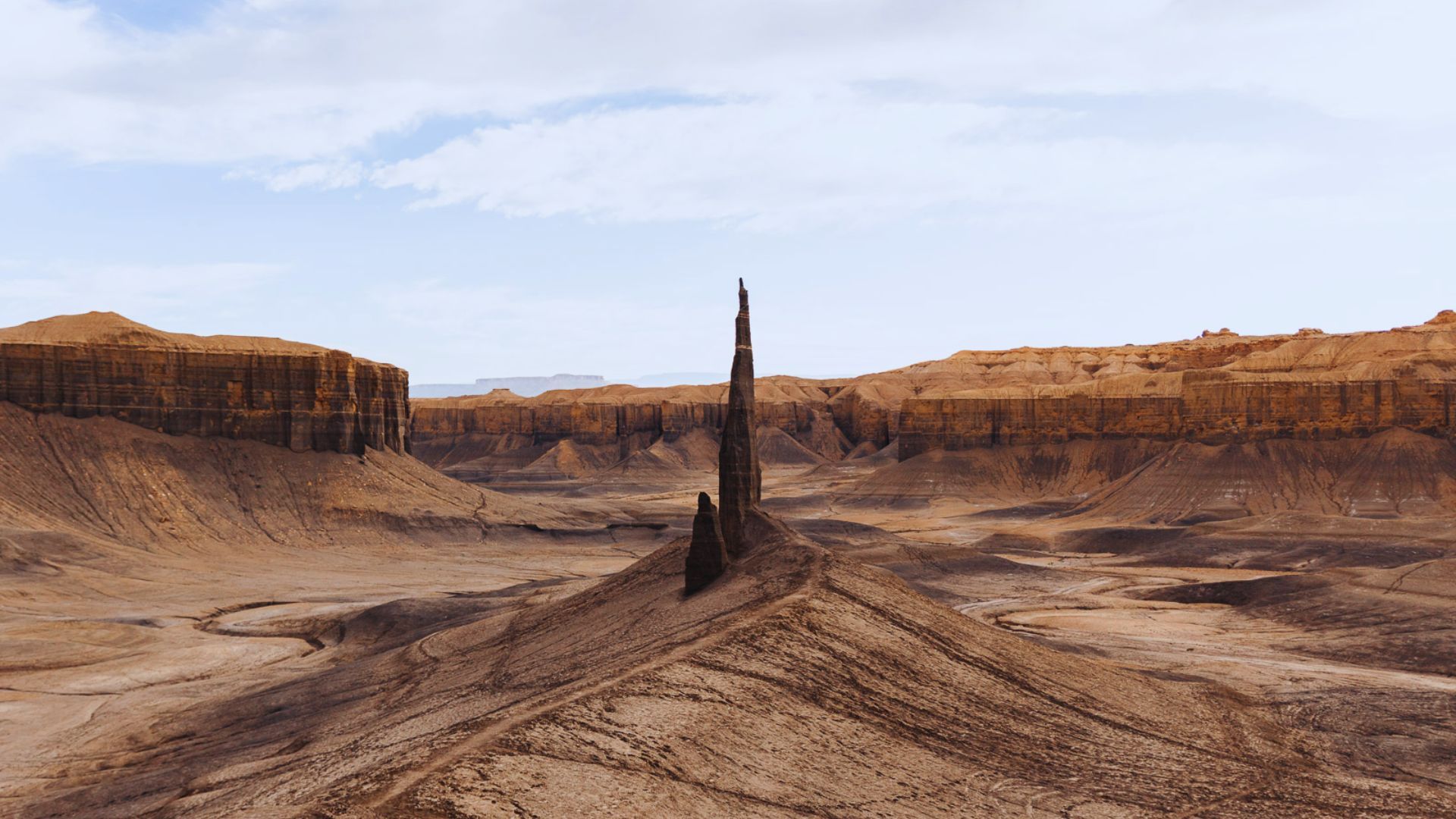 A solitary tower rises in the center of a barren desert, surrounded by endless sand dunes.