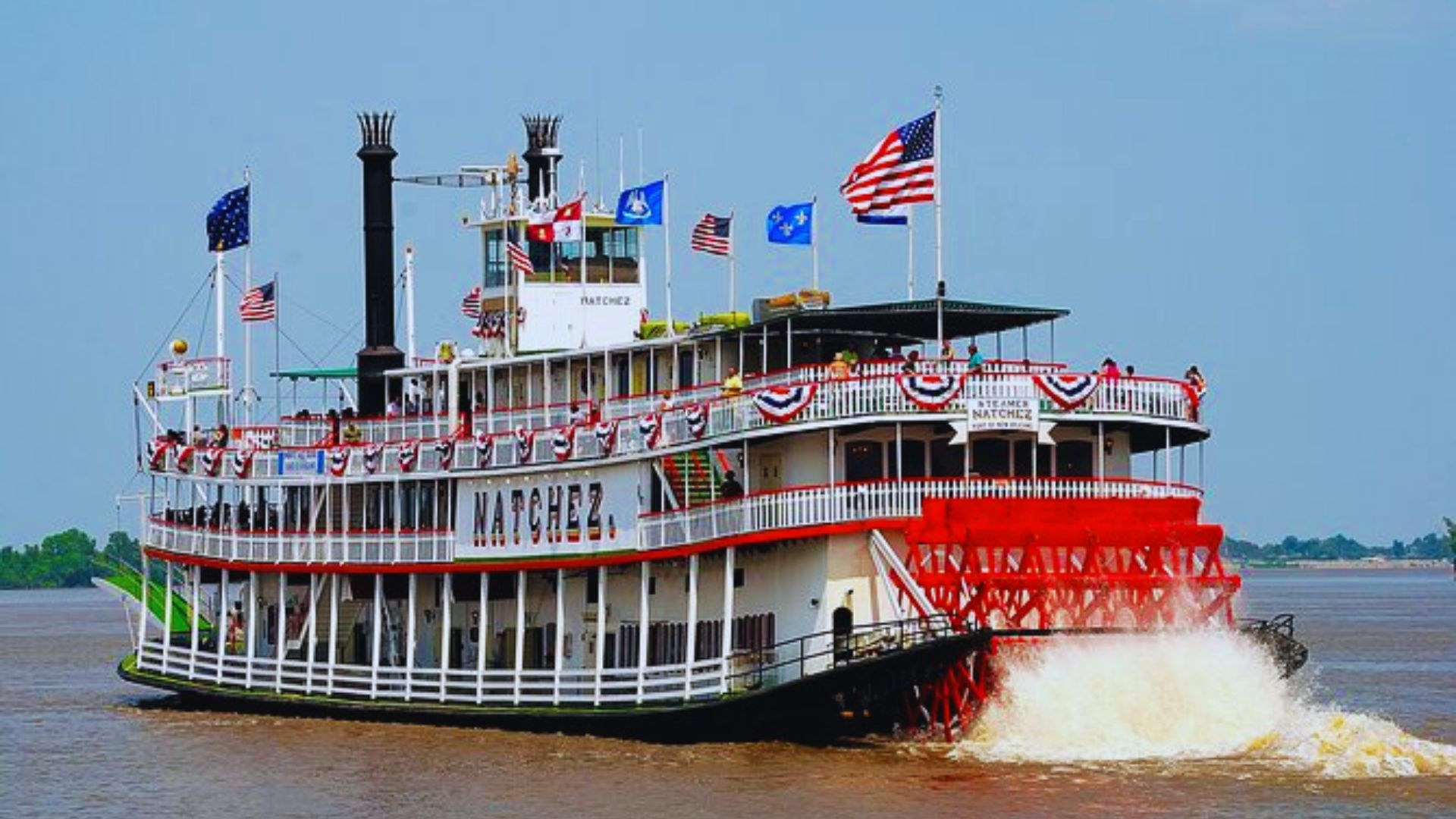 A riverboat gliding smoothly down a tranquil river, surrounded by lush greenery and clear blue skies.