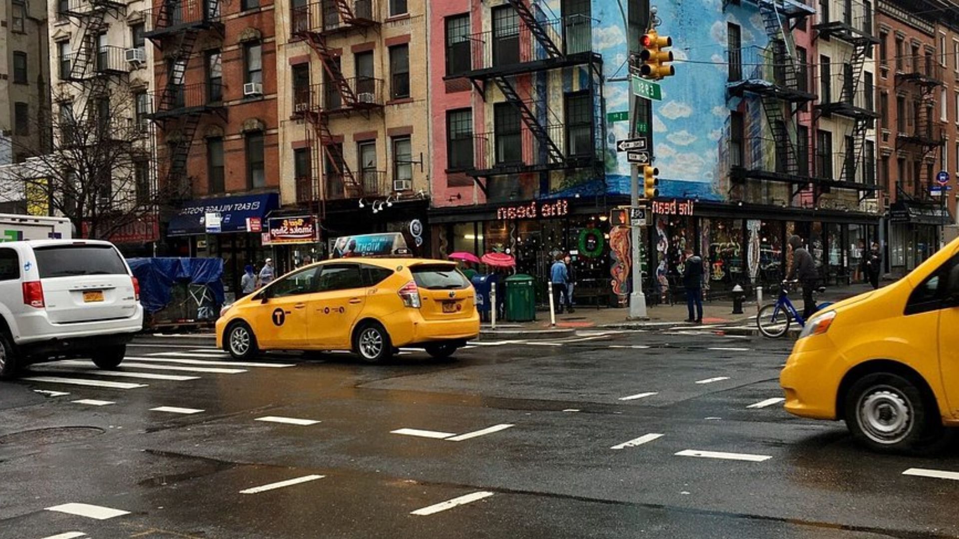 A yellow taxi cab is parked at a busy intersection, waiting for passengers amidst city traffic.