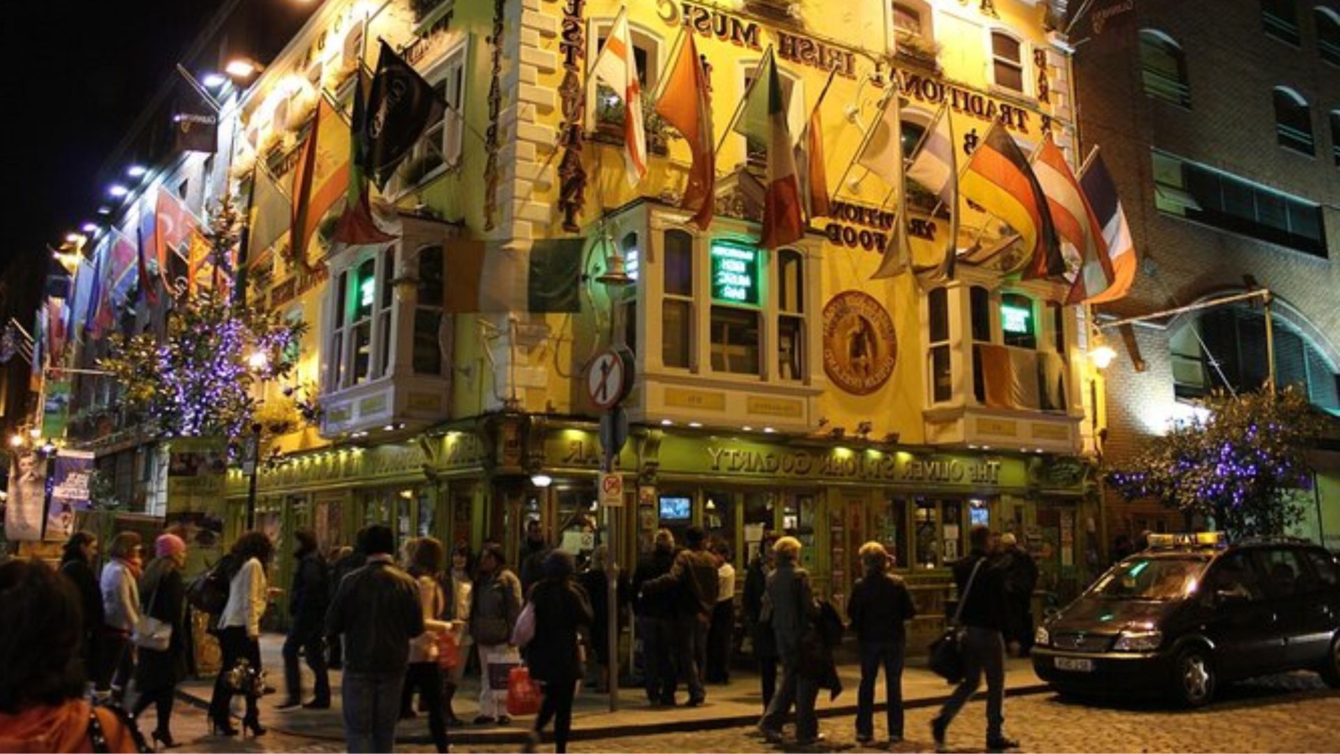 A group of people stands outside a pub at night, illuminated by streetlights and the pub's warm glow.