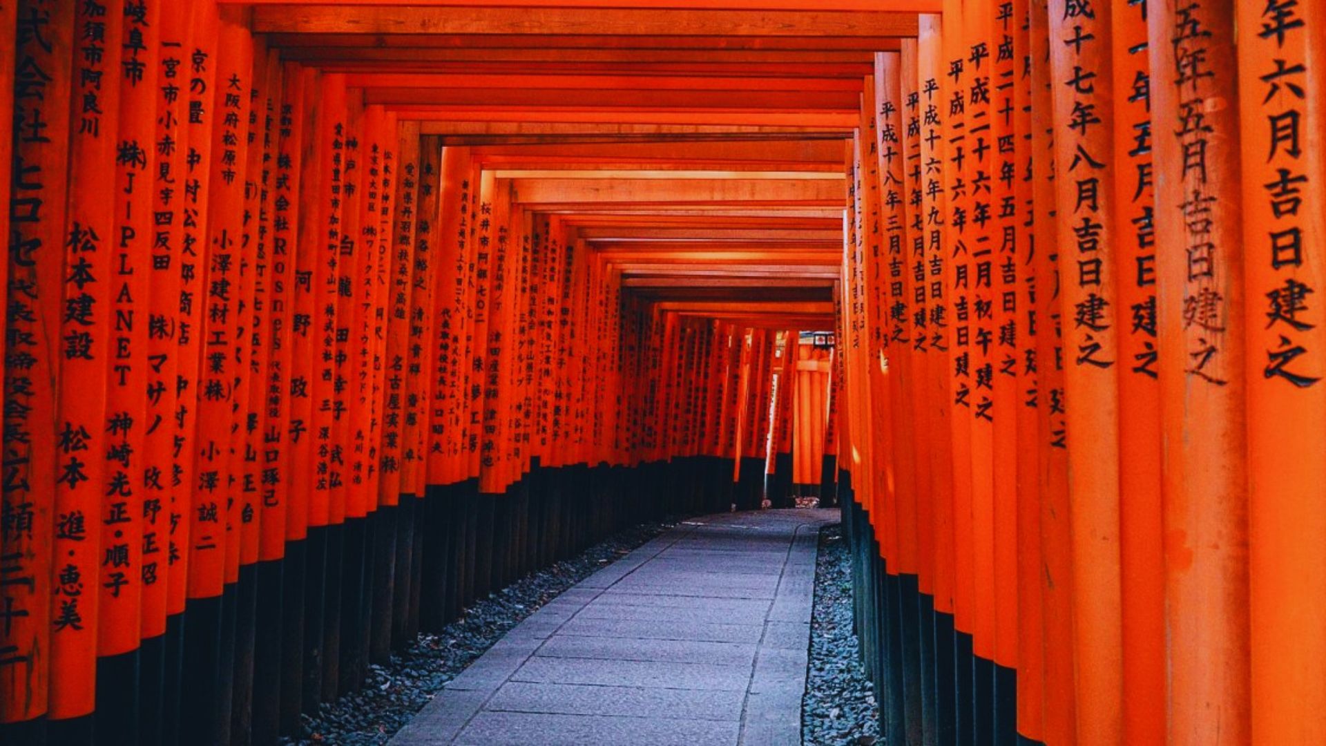 A serene walkway adorned with vibrant orange torii gates, creating a picturesque path through a tranquil landscape.