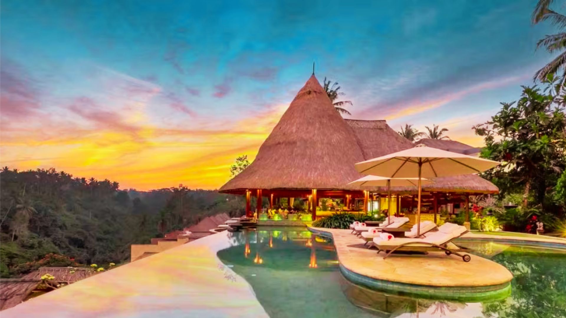 A luxurious tropical retreat at sunset with a thatched-roof villa, infinity pool, and sun loungers. The vibrant sky creates a serene, relaxing ambiance.