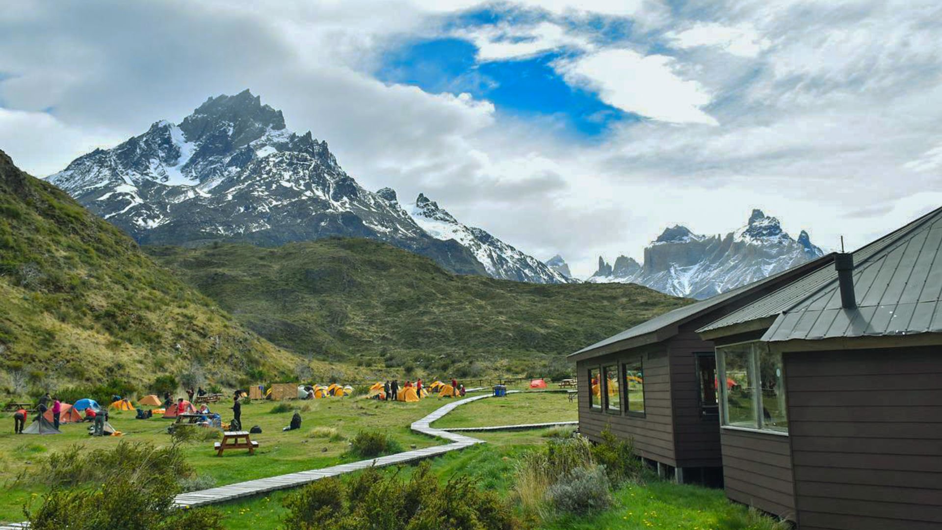 A group of people relaxes outside a mountain cabin, surrounded by trees and scenic views.