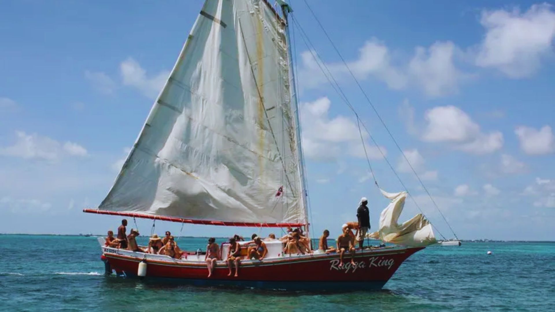 A sailboat with several people sailing on the ocean, surrounded by blue water and a clear sky.