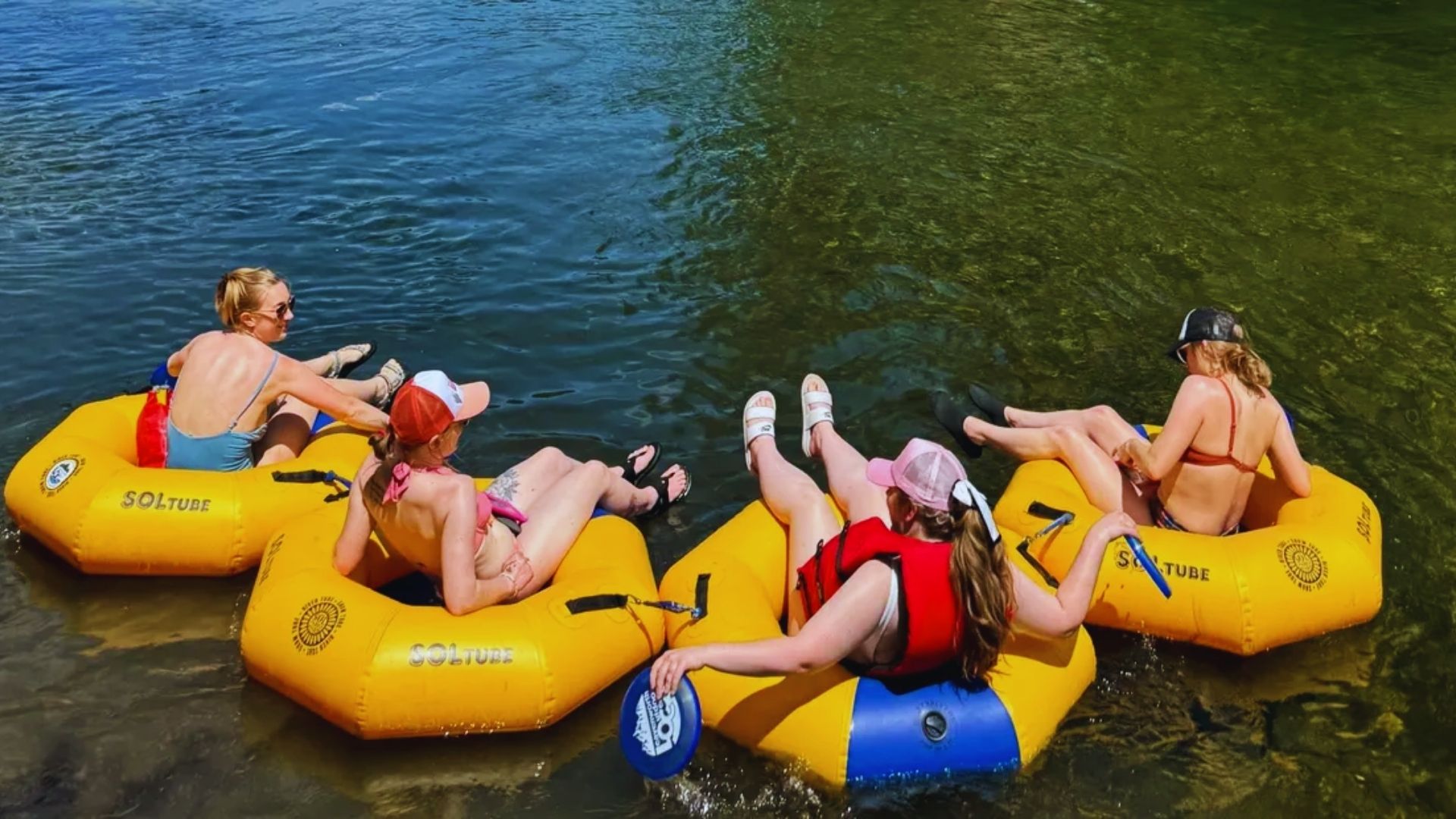 Three individuals relax on yellow inflatable tubes floating in the water under a clear blue sky.