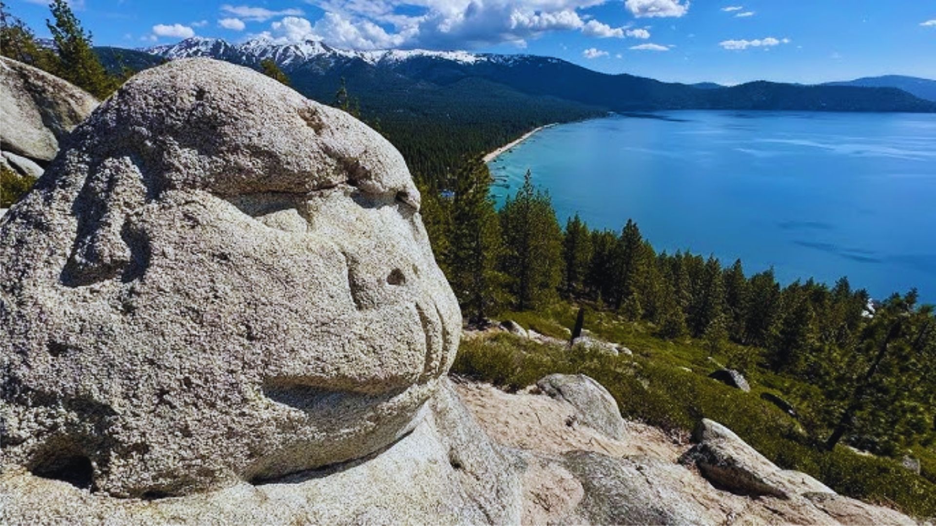 A large rock with a carved face overlooks a vast ocean under a clear blue sky.
