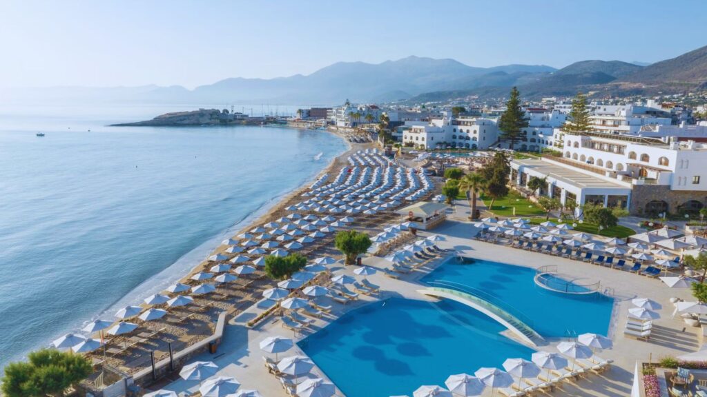 A serene beach view at a hotel in Crete, featuring golden sand and clear blue waters under a bright sky.
